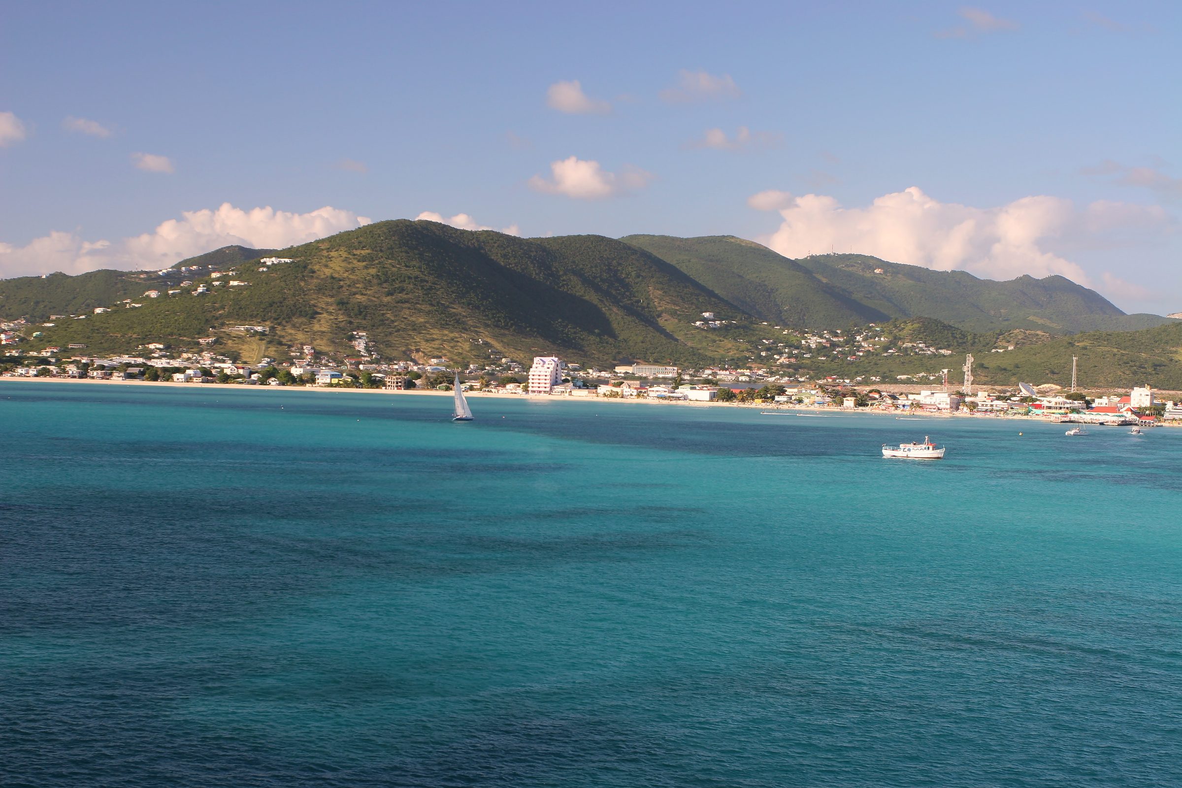 Coastal town on a bright turquoise bay with green hills beyond.