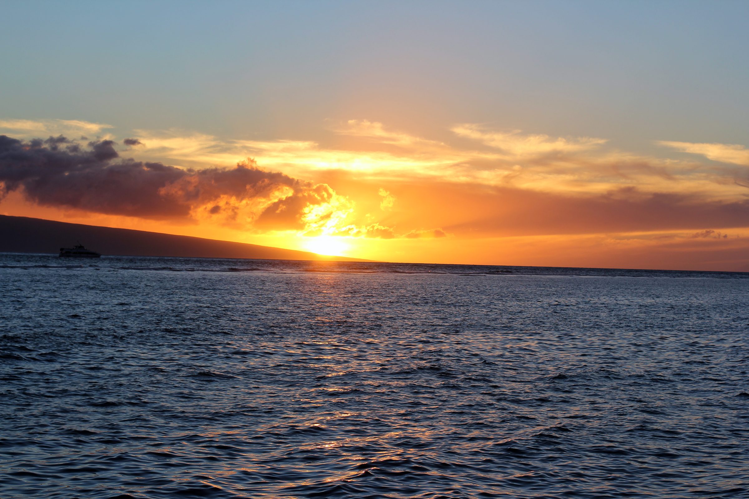 Bright sun touching the ocean horizon with a small boat silhouette.