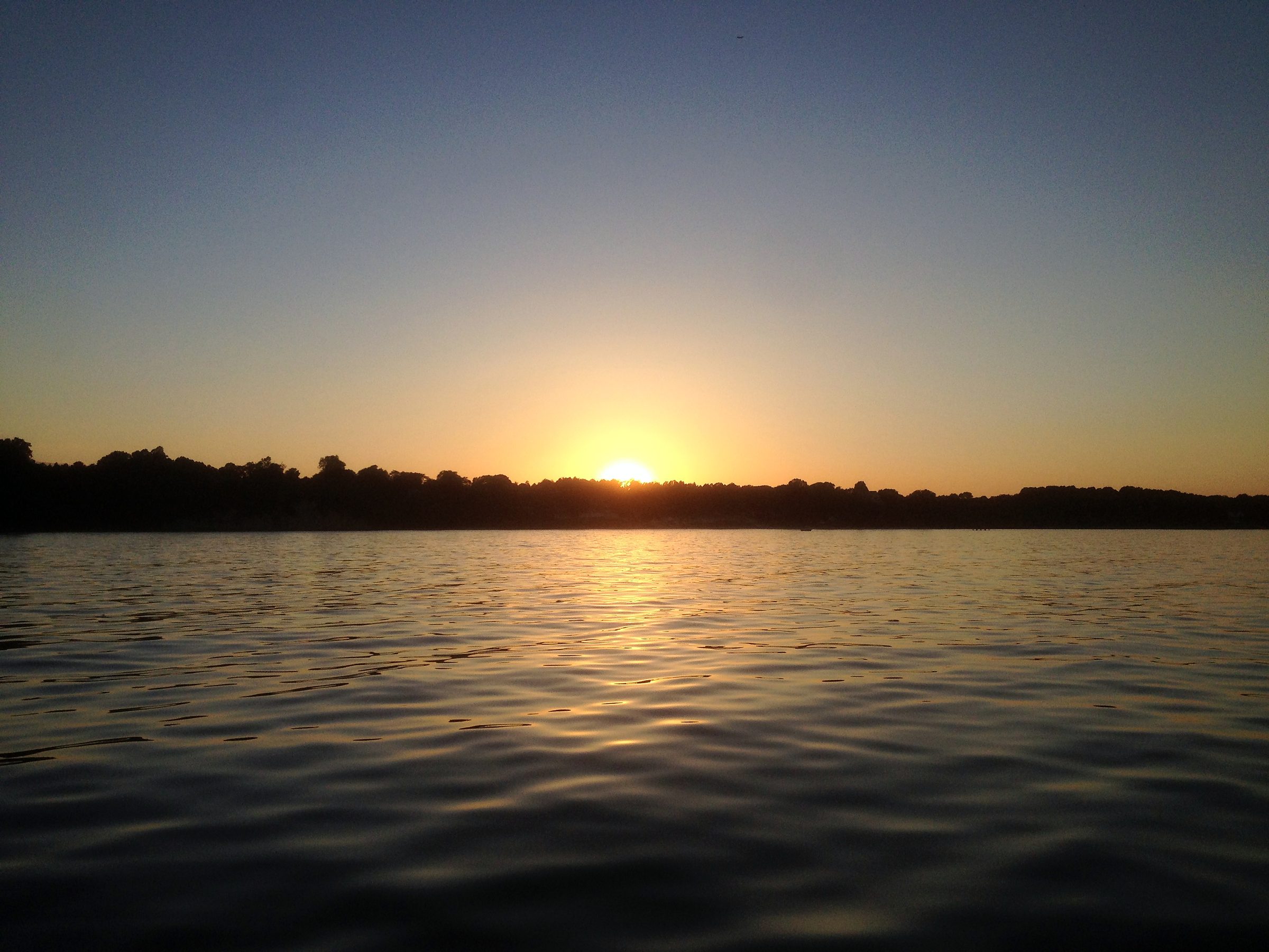 Sun centered on the water horizon, treeline eating the day.