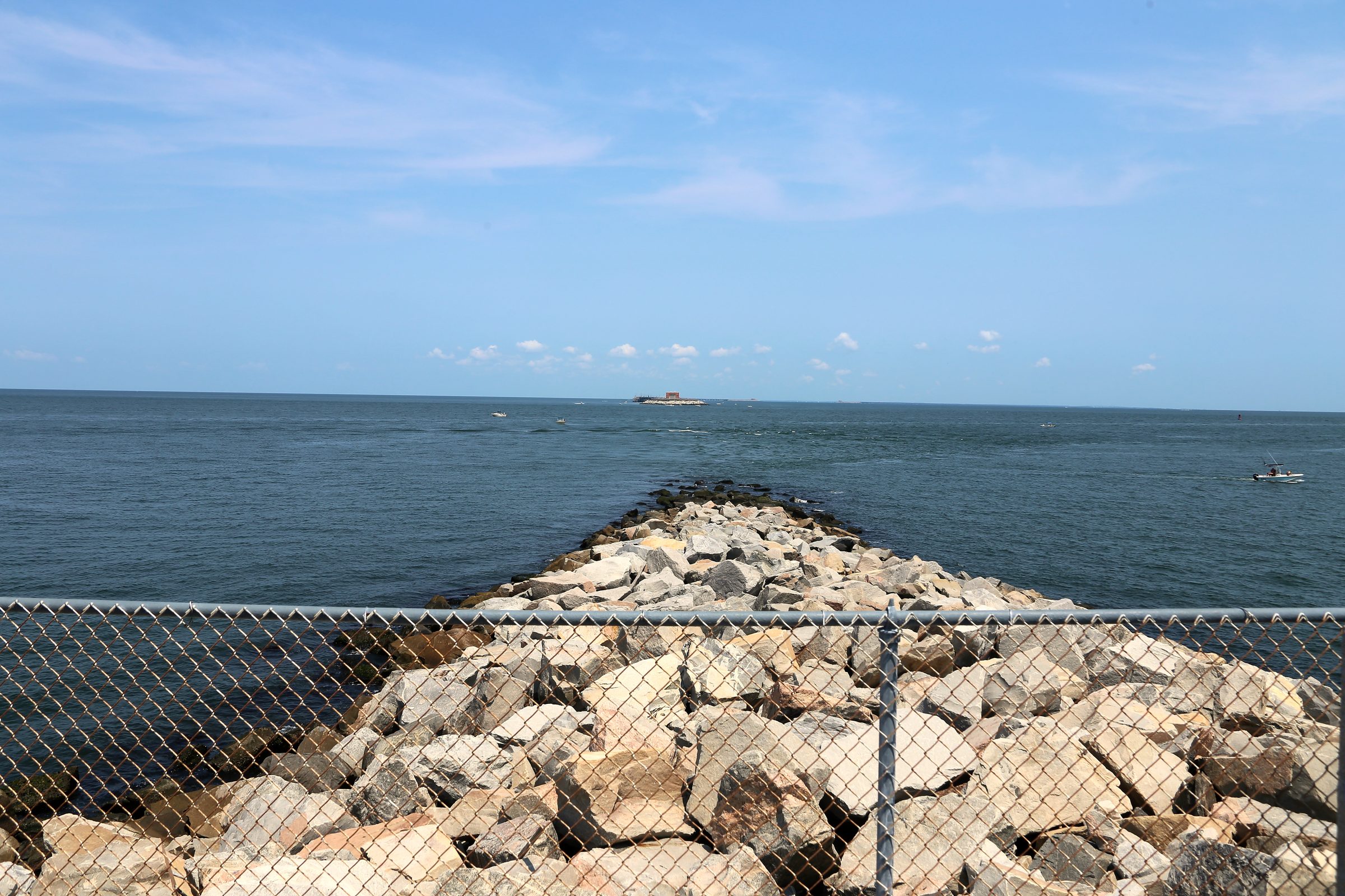 Stone jetty aiming at a small island across blue water.
