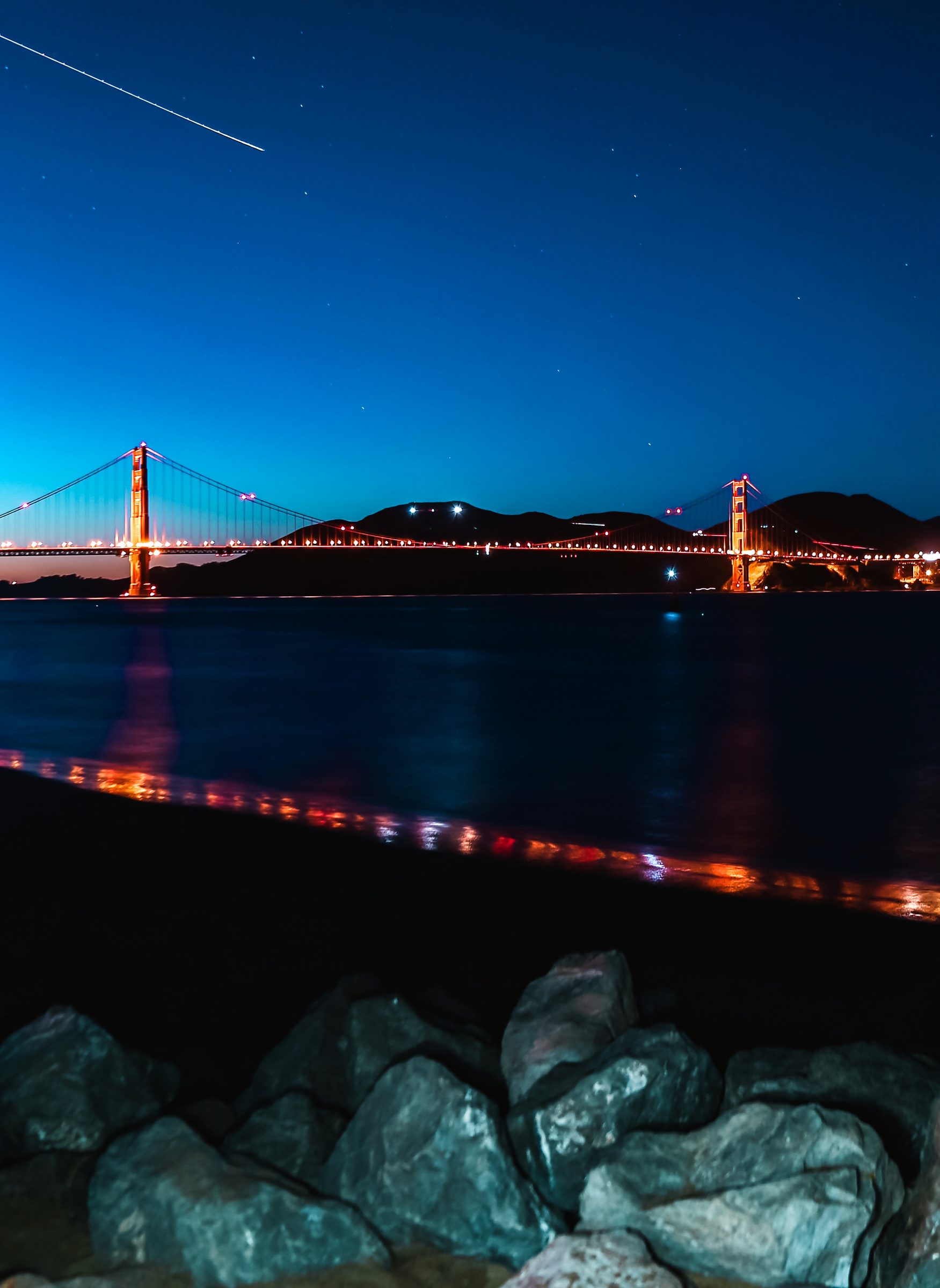 Blue foreground rocks under the illuminated Golden Gate at dusk.