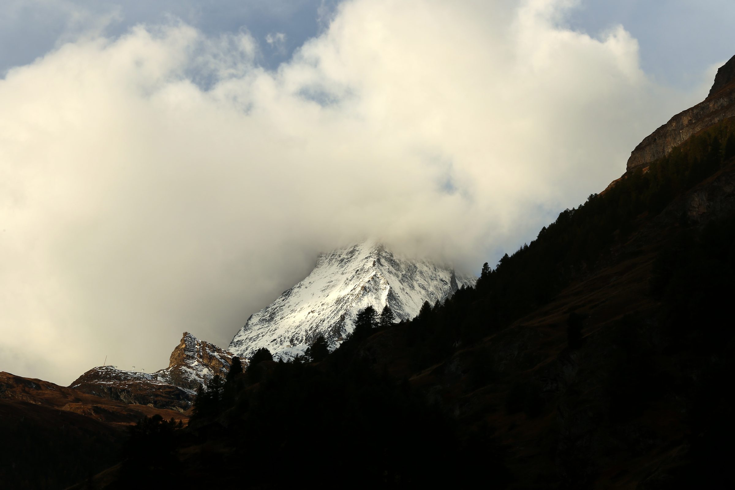 Forested hill silhouette with a sunlit peak glowing through cloud.