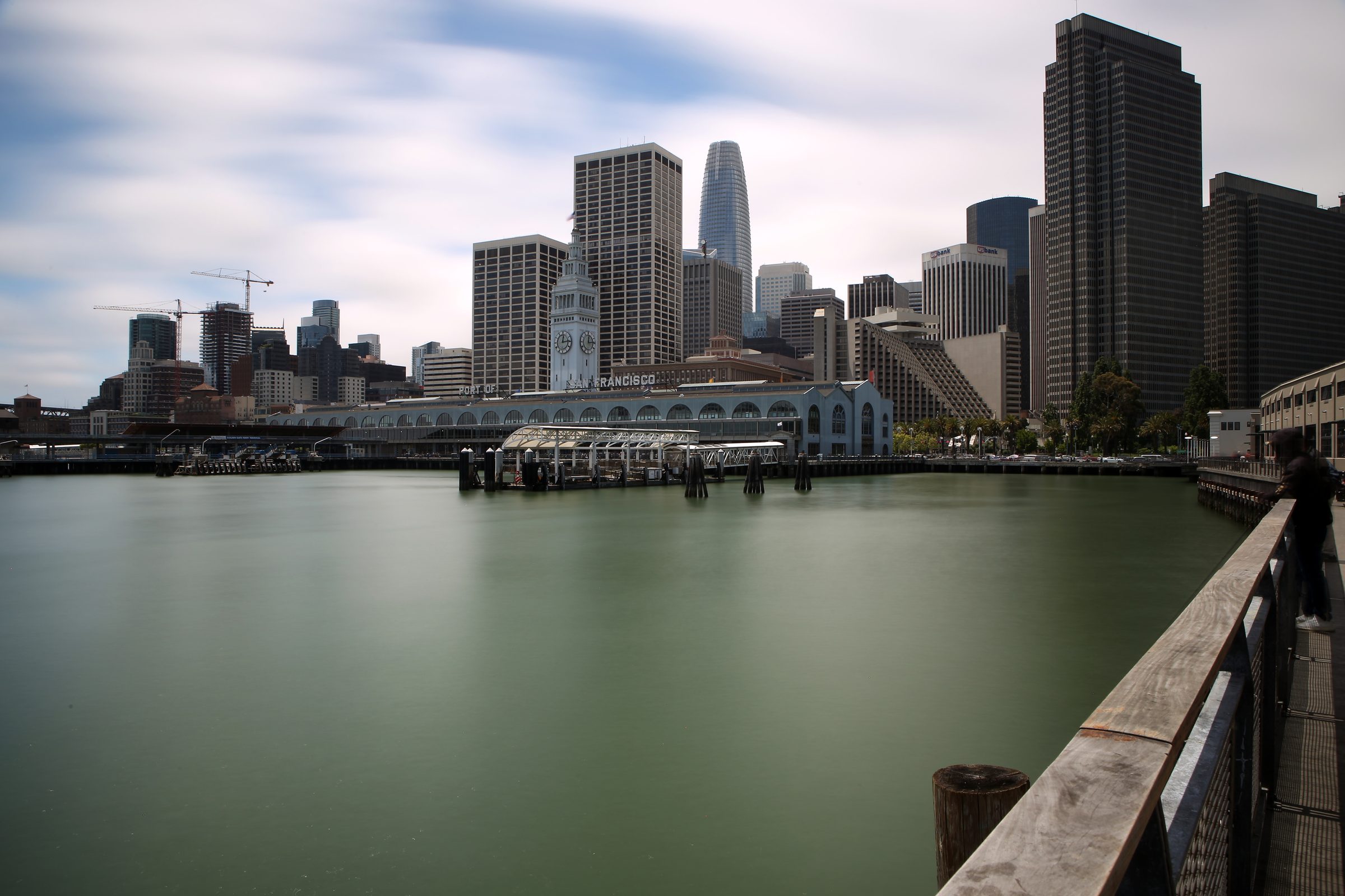 City skyline and clock tower across soft green river water.