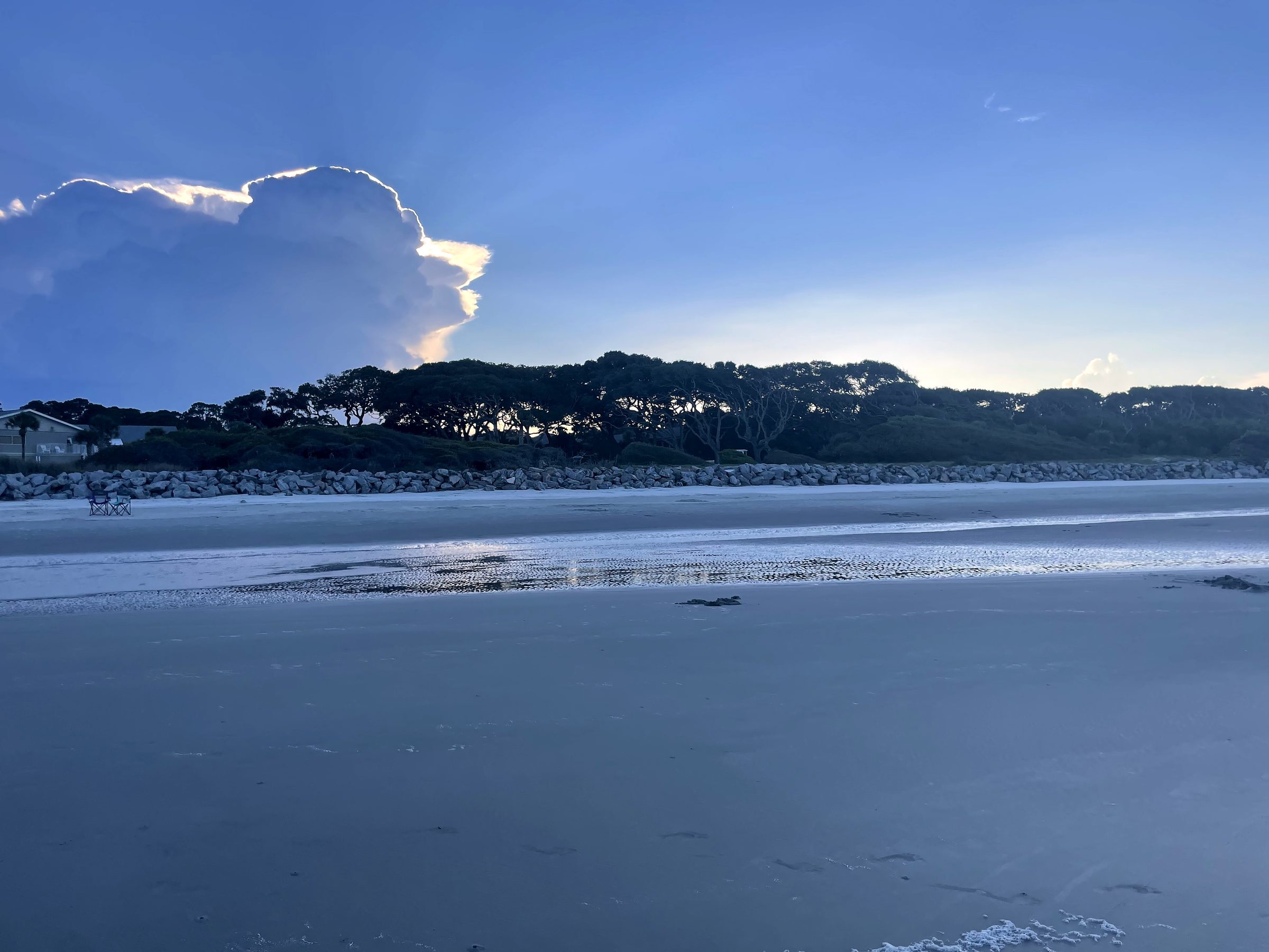 Wide low-tide beach with sandbars under deep cloudy blue sky.