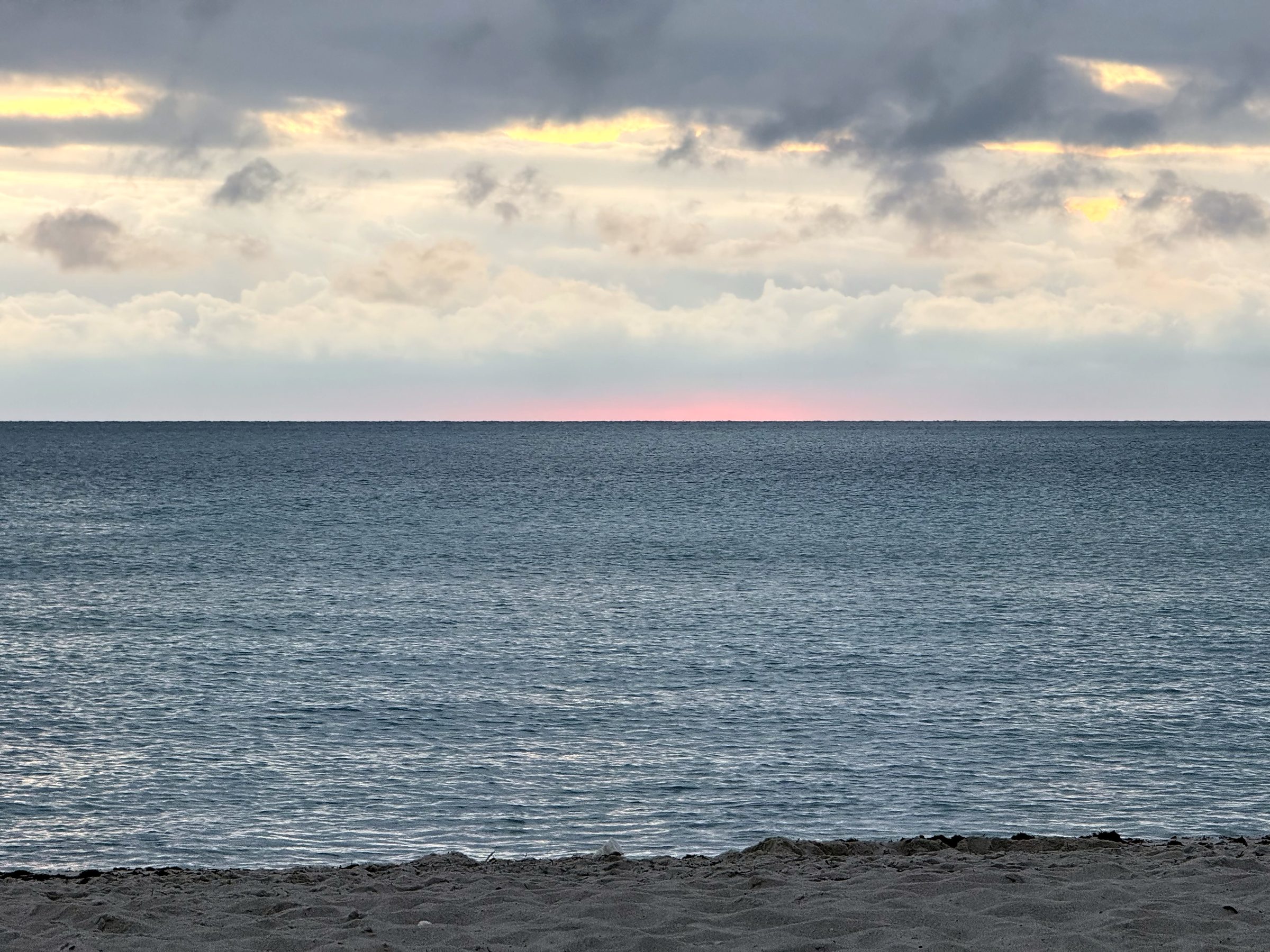 Calm grey-blue sea and sandy beach under a pale cloudy sky.