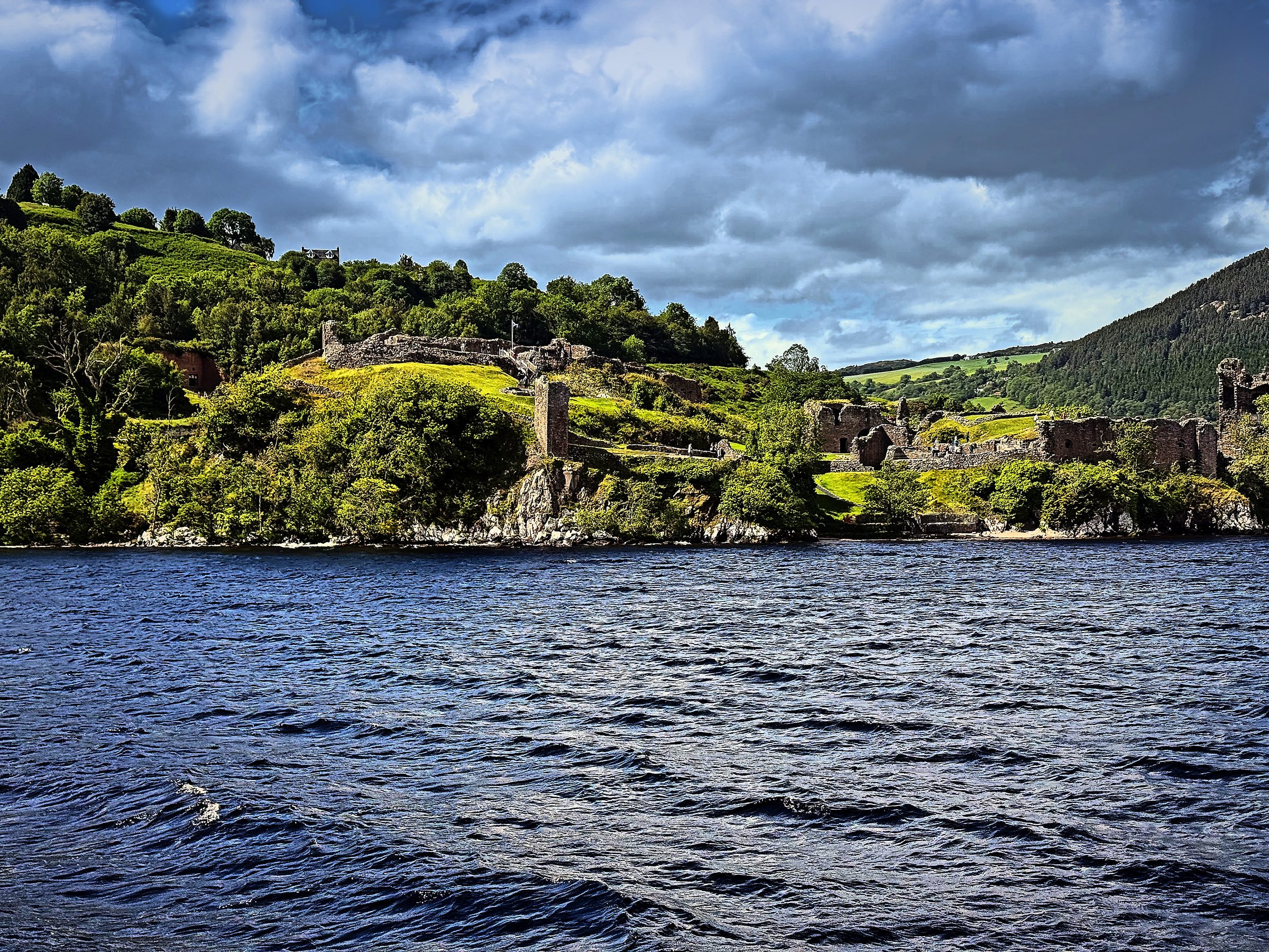 Ruined stone tower on a green hill over dark blue water.
