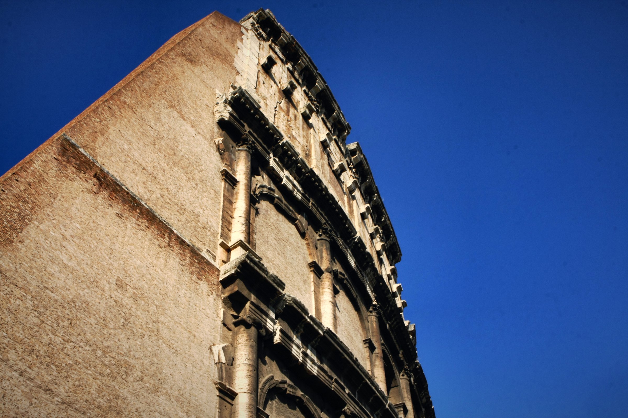 The outer wall of the Colosseum sweeping up into a deep blue sky.