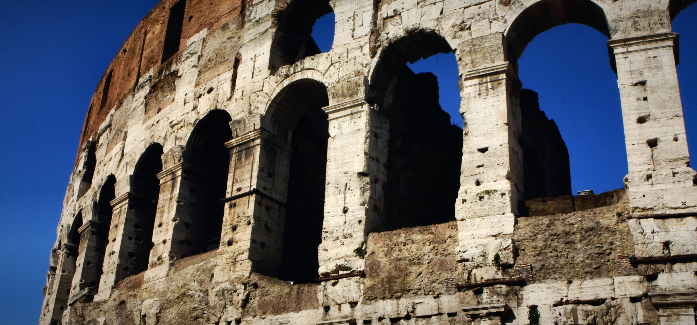 The Colosseum's upper arches with blue sky showing through.