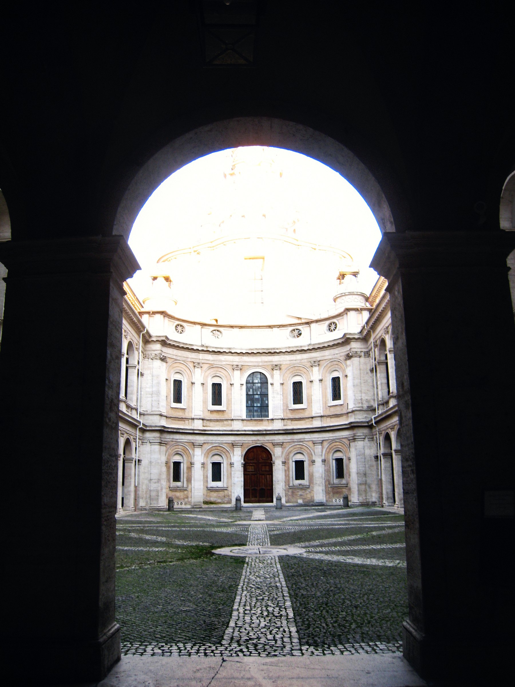 A dark archway framing a sunlit courtyard with an arcade beyond.