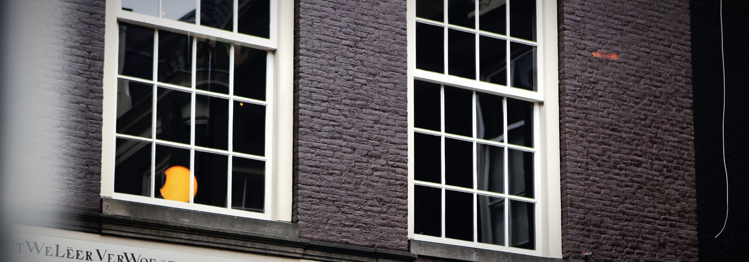 A dark brick facade with white sash windows and a single lit pane.