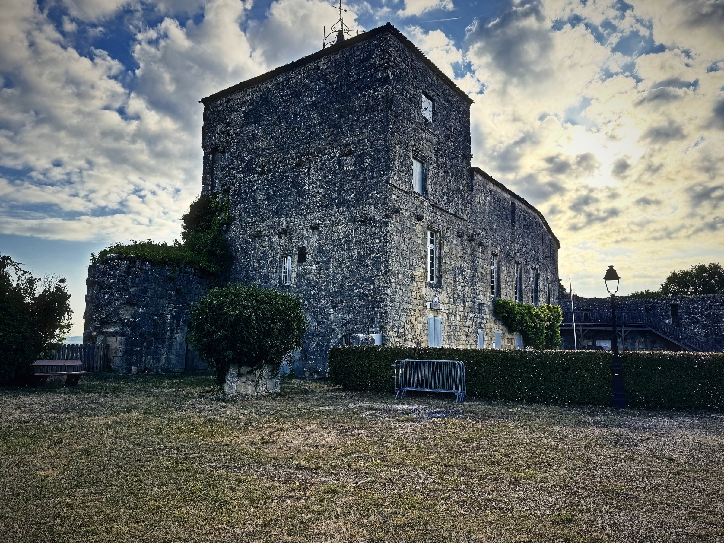A square stone keep and its outbuildings under a dramatic sky of broken cloud.
