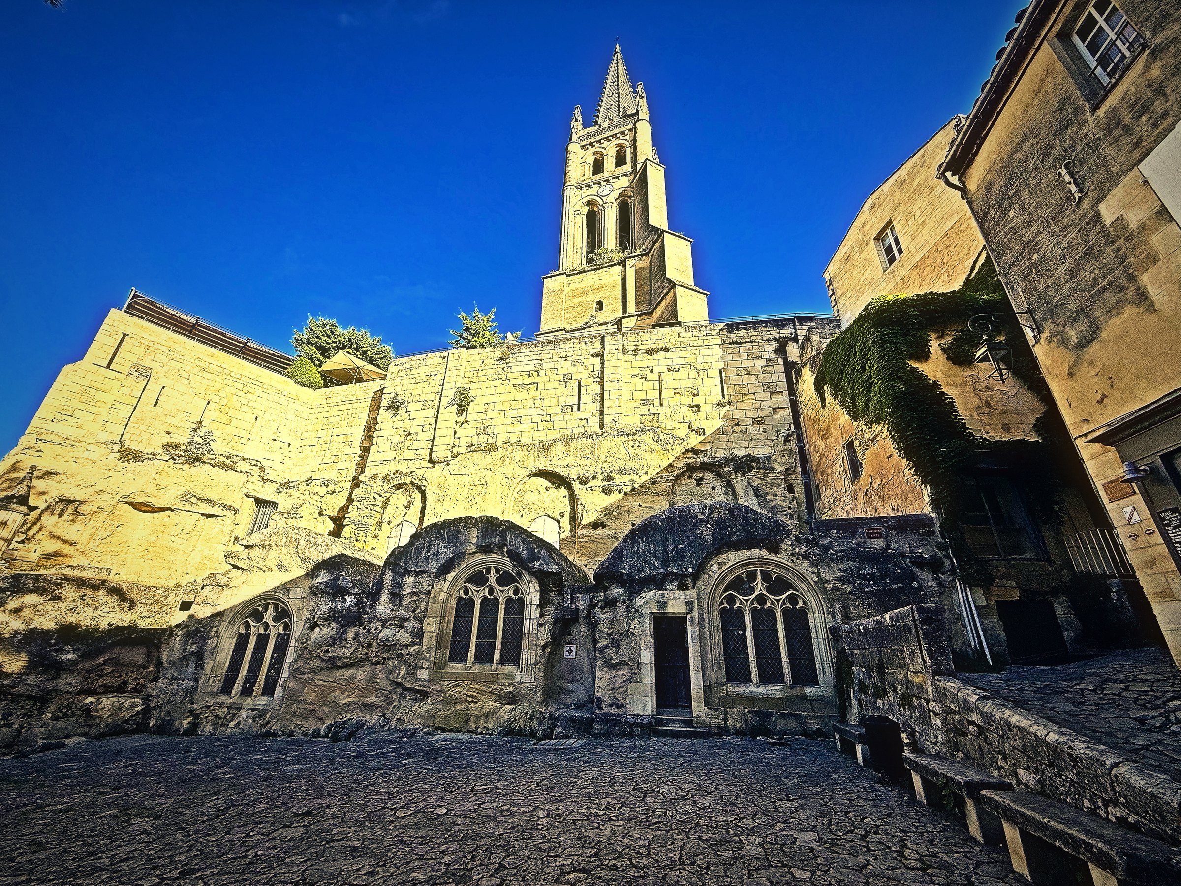 The rock-cut walls and arches of Saint-Émilion's Monolithic Church beneath its tall bell tower in morning sun.