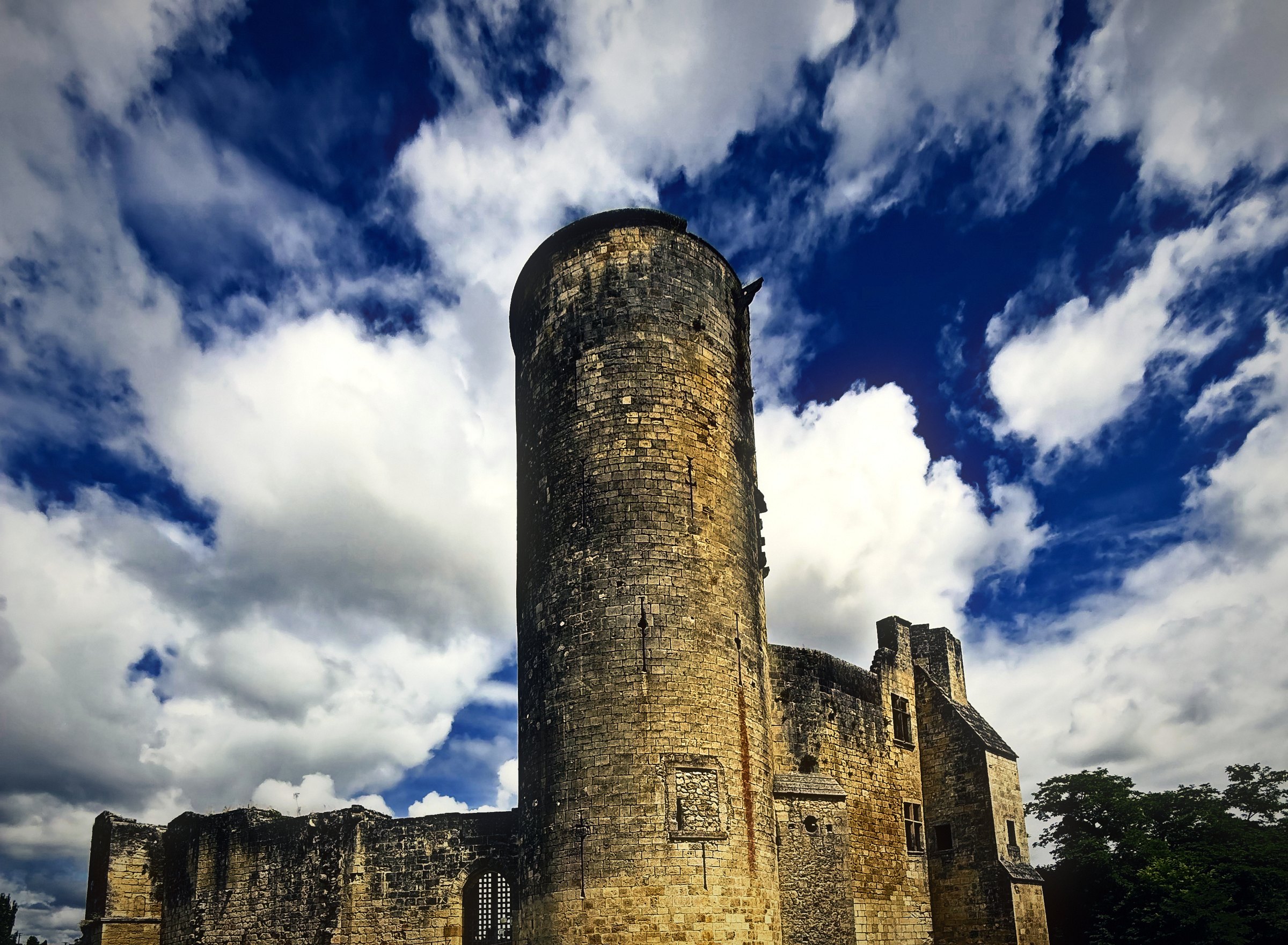 The tall round keep of a ruined castle rising against towering white clouds and deep blue sky.