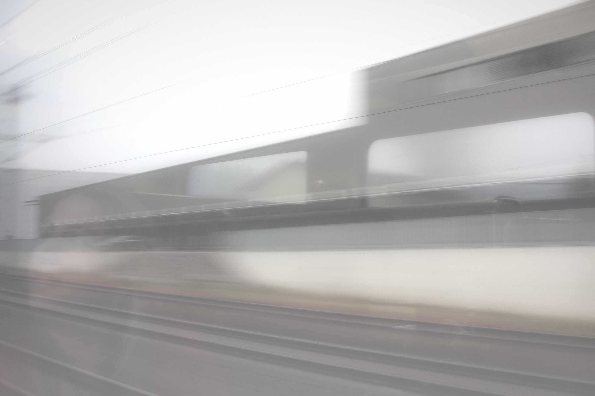 Washed-out blur of a station platform and a low building in near-white.