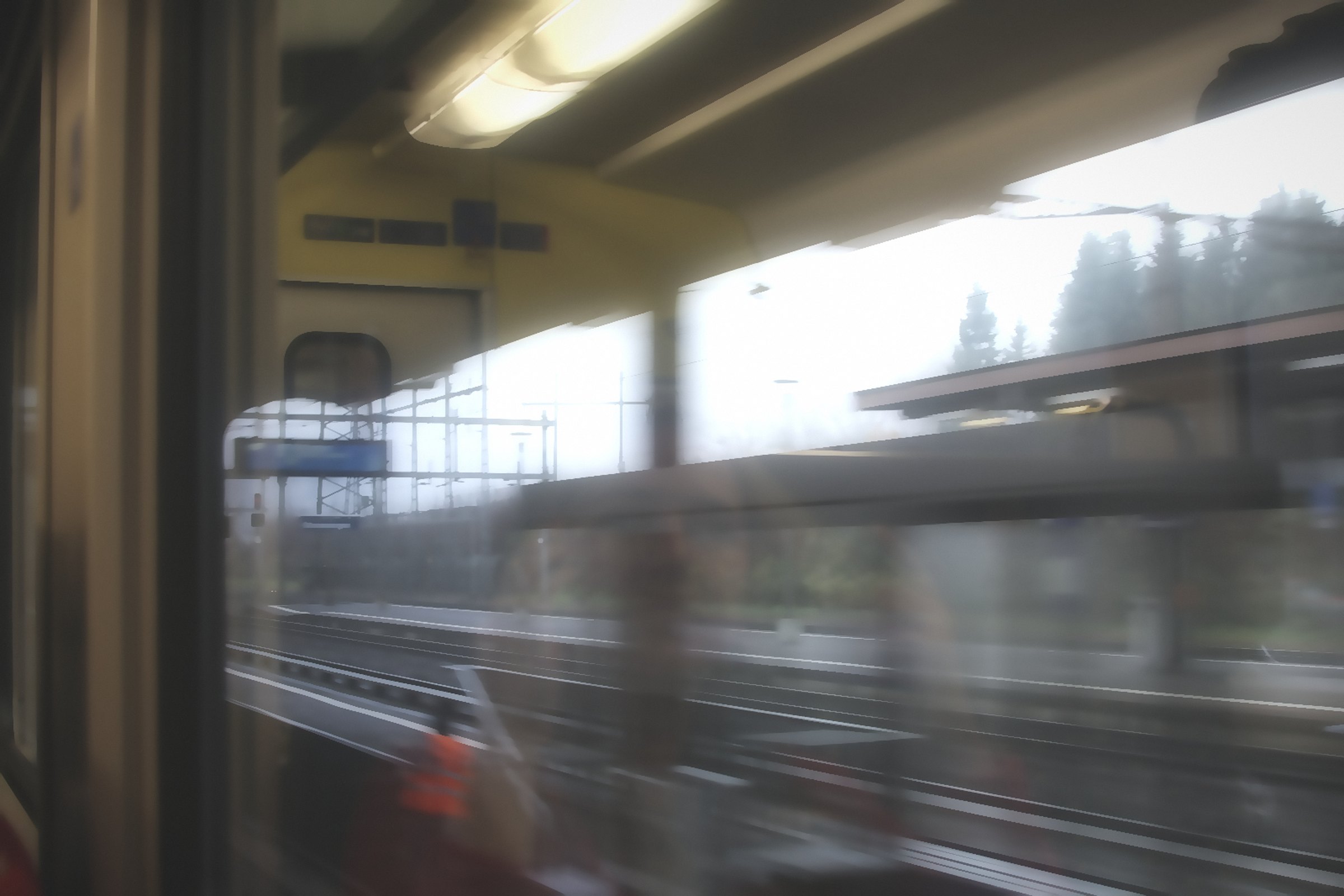 Hazy view through a train window with a ceiling light and a passing station.