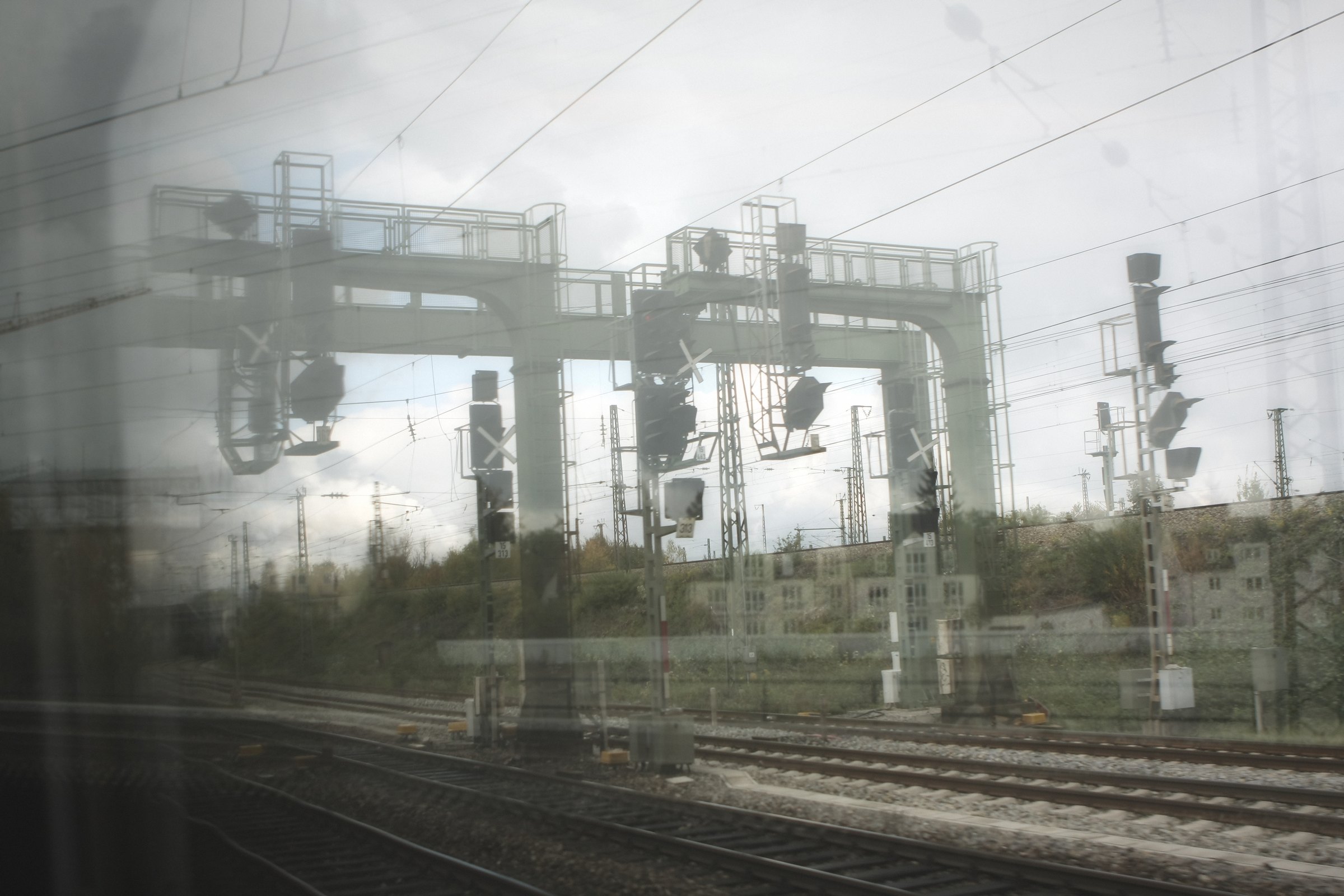 Double-exposed signal gantries and overhead wires over pale tracks.