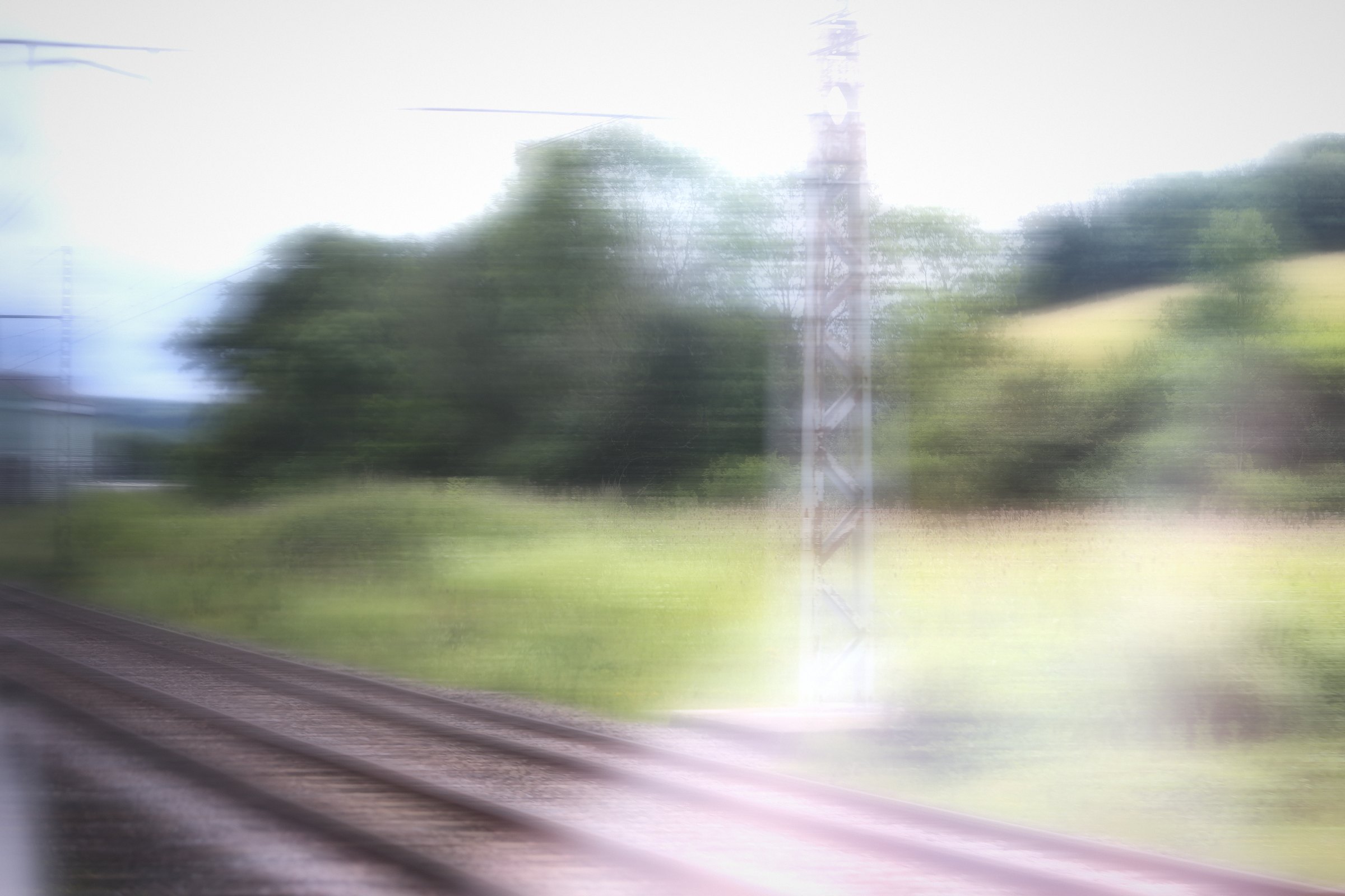 Pale motion blur of green fields and a pylon beside the tracks.