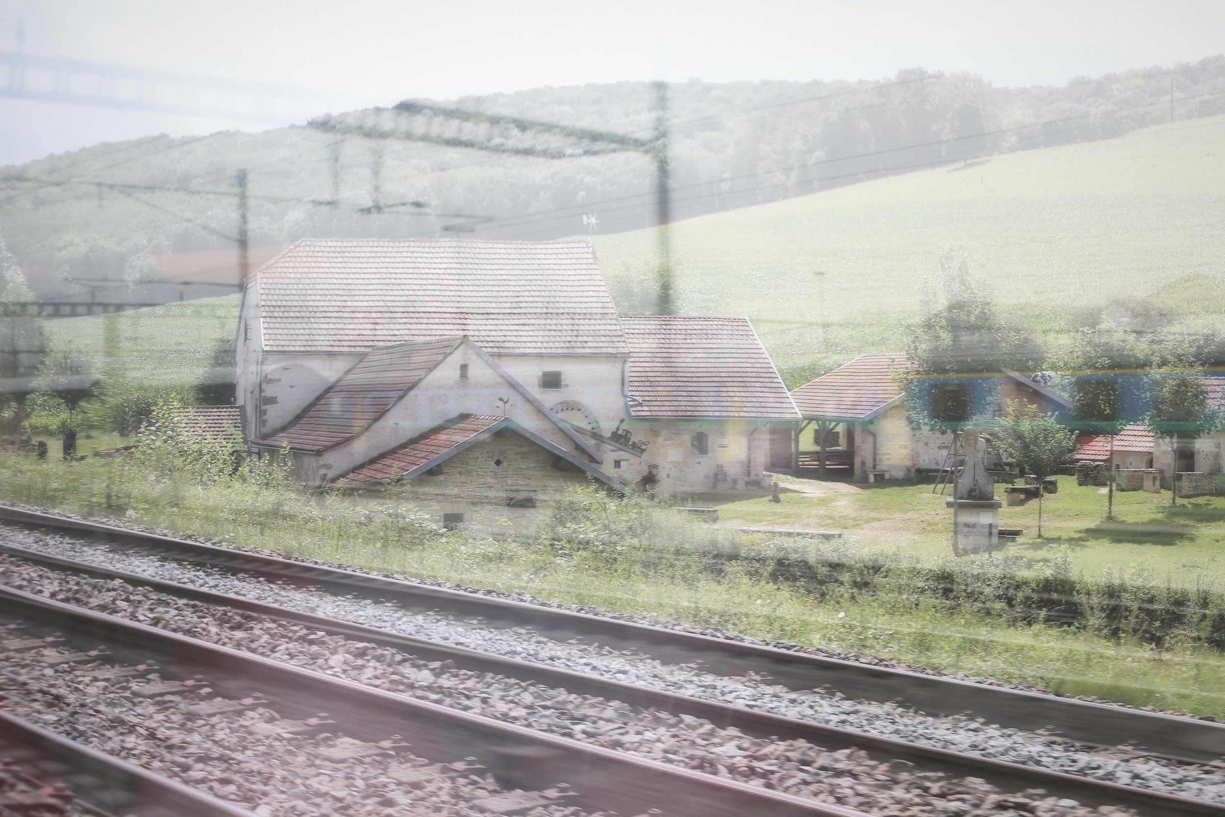 Double exposure of a farm village, fields and railway tracks in soft light.
