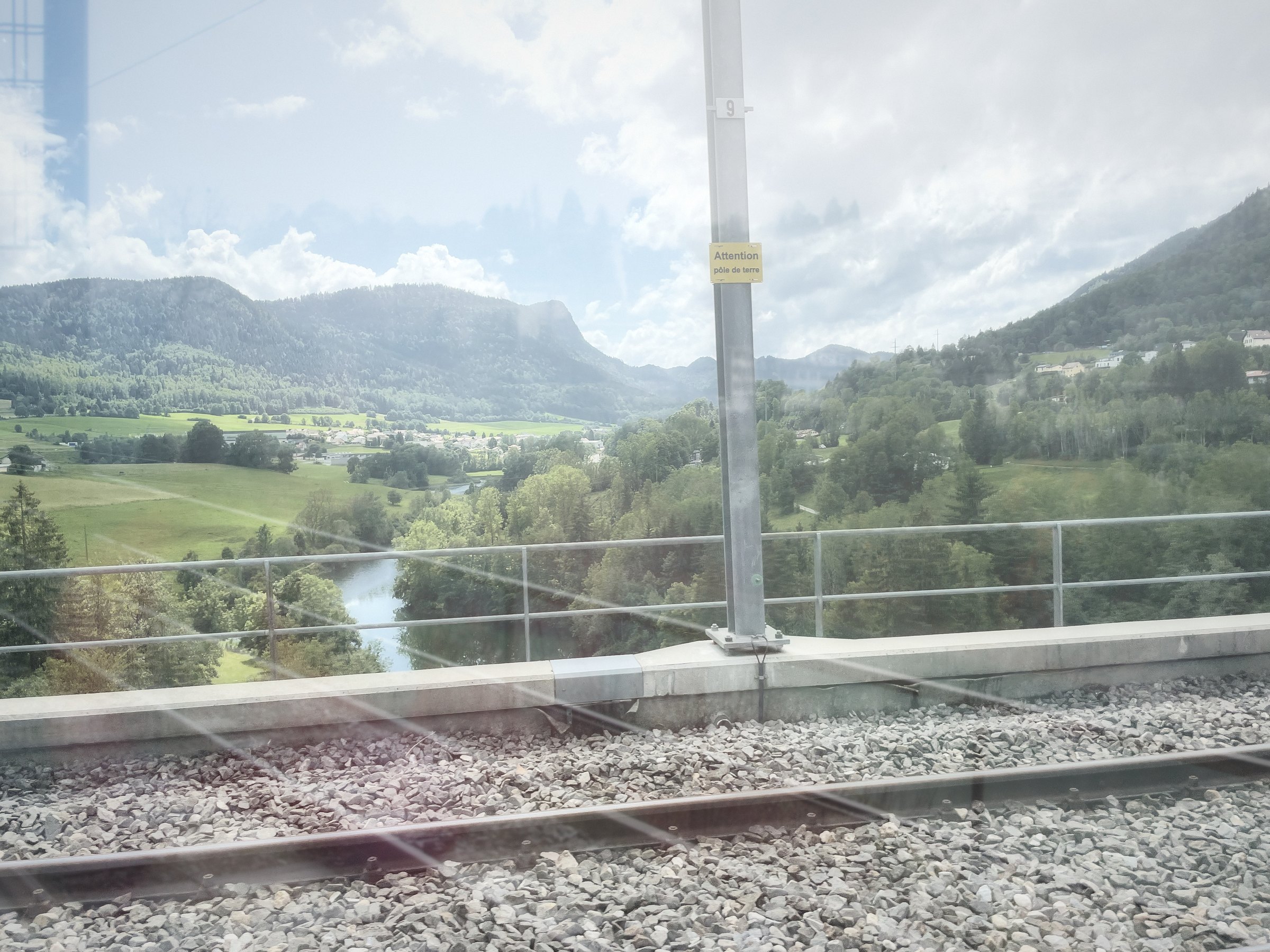 Double exposure of a green valley with a river, railing and tracks.