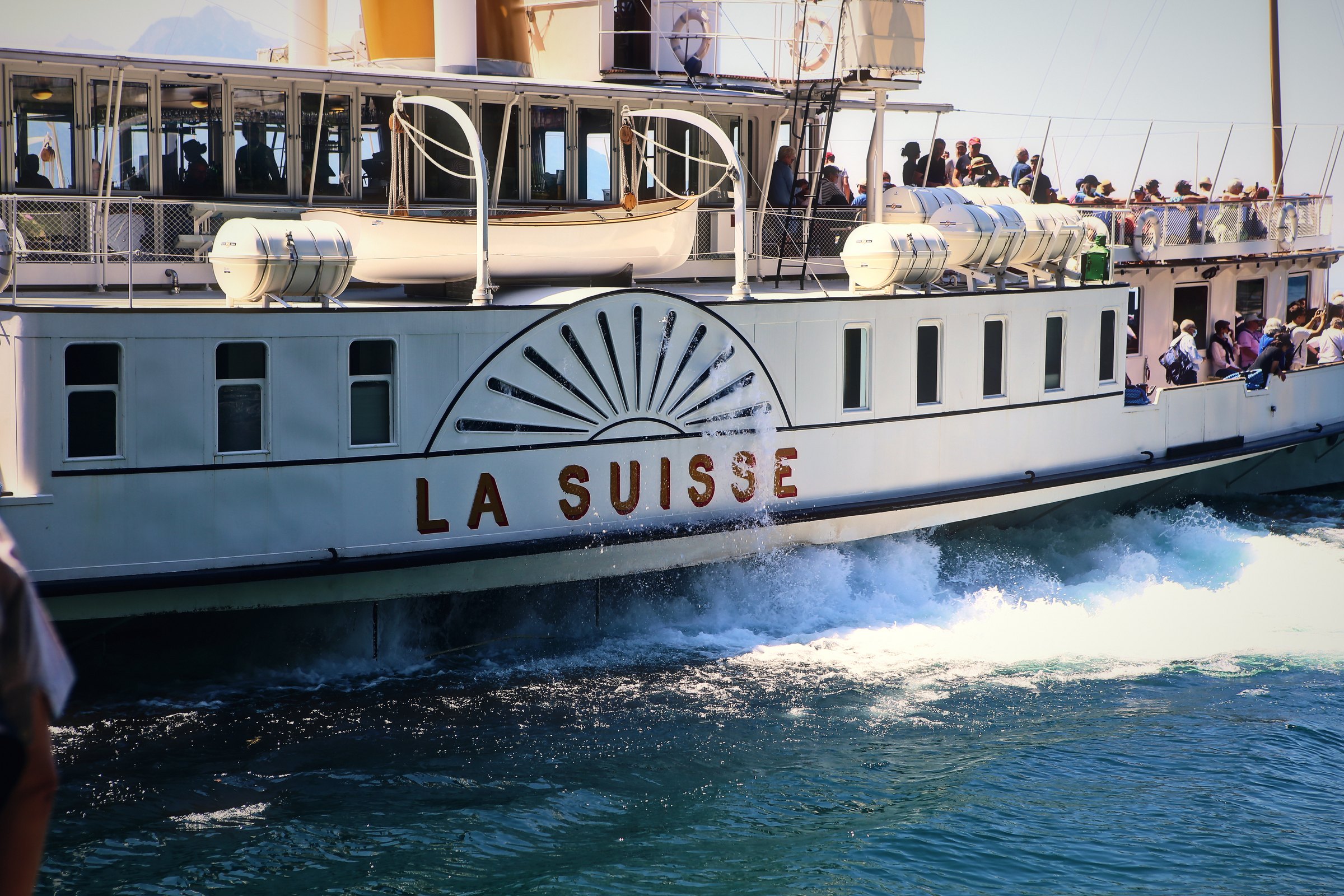 White paddle steamer La Suisse with a gilded sunburst paddlebox churning up white water.