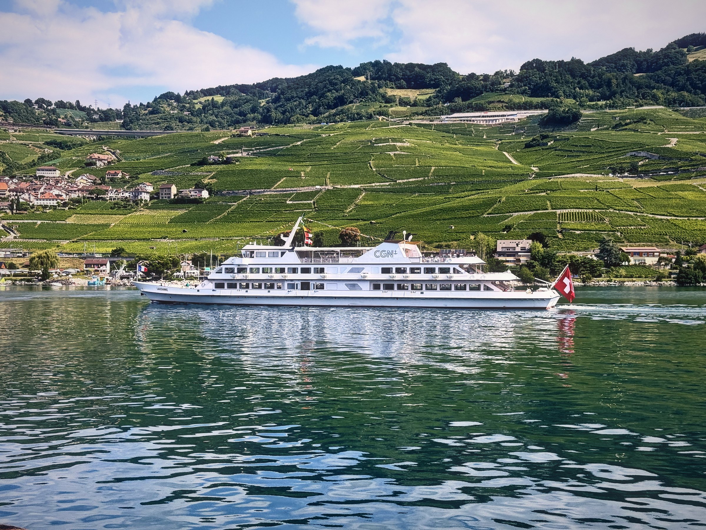 White lake ferry gliding below green vineyard terraces on Lake Geneva.