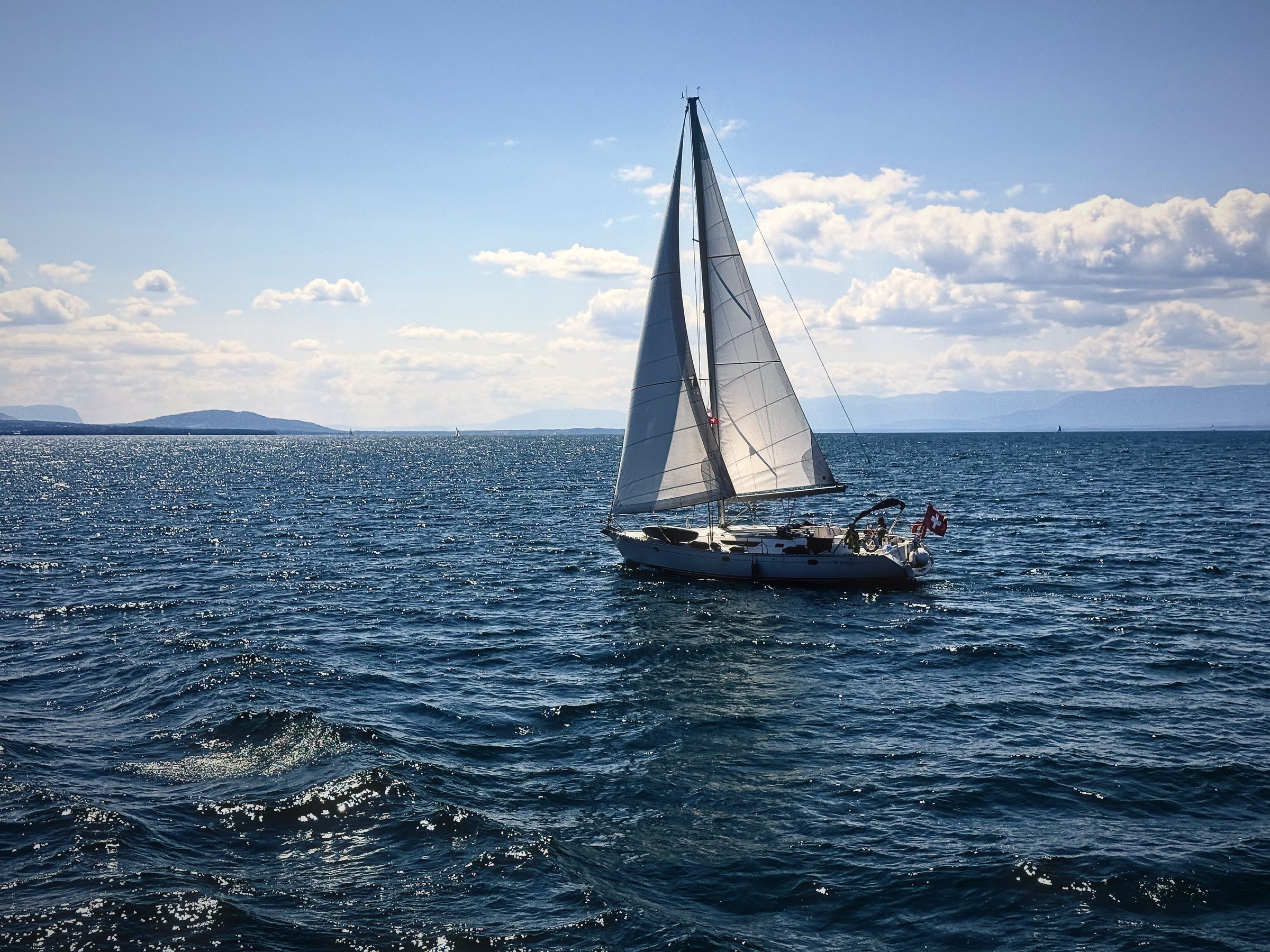 Sailboat heeling in the breeze on deep blue Lake Geneva under summer clouds.