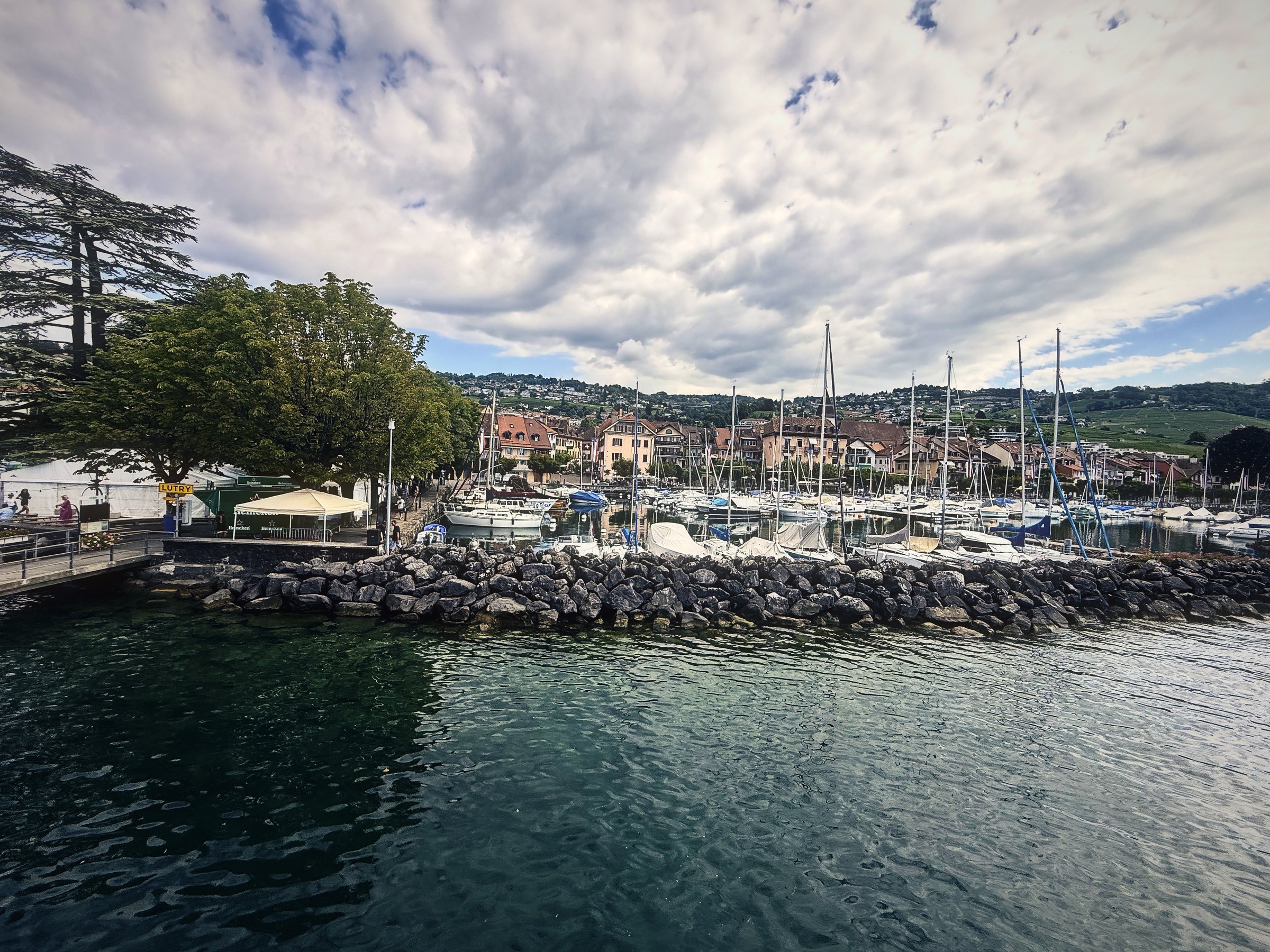 Small harbor with sailboat masts behind a rock breakwater under towering summer clouds.
