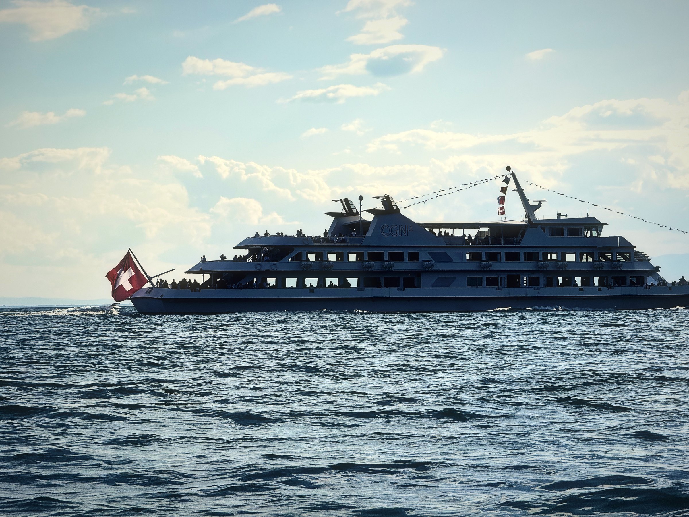 Sleek white lake cruiser with a Swiss flag sailing in early evening light.