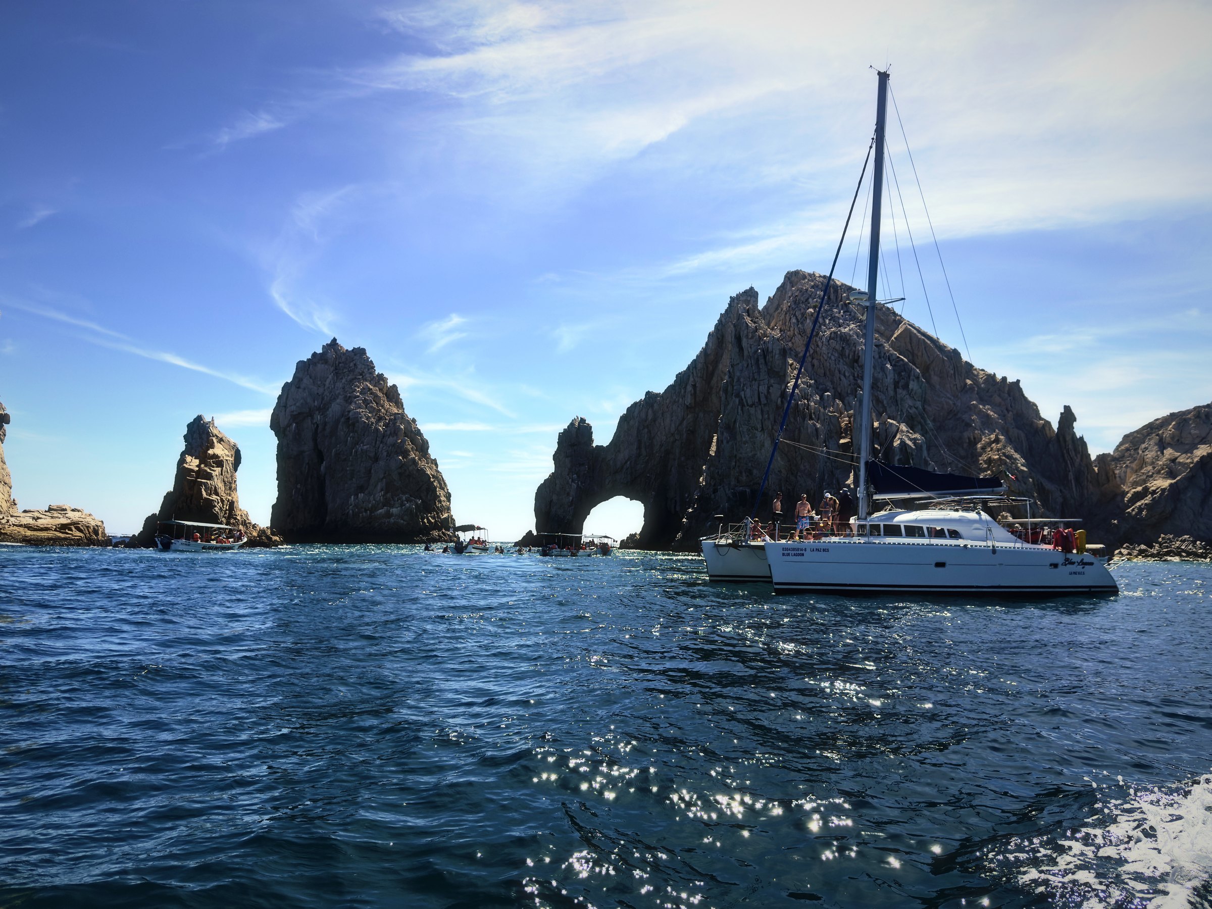 Sailboat at anchor near tall granite rocks and a natural arch under a blue sky.