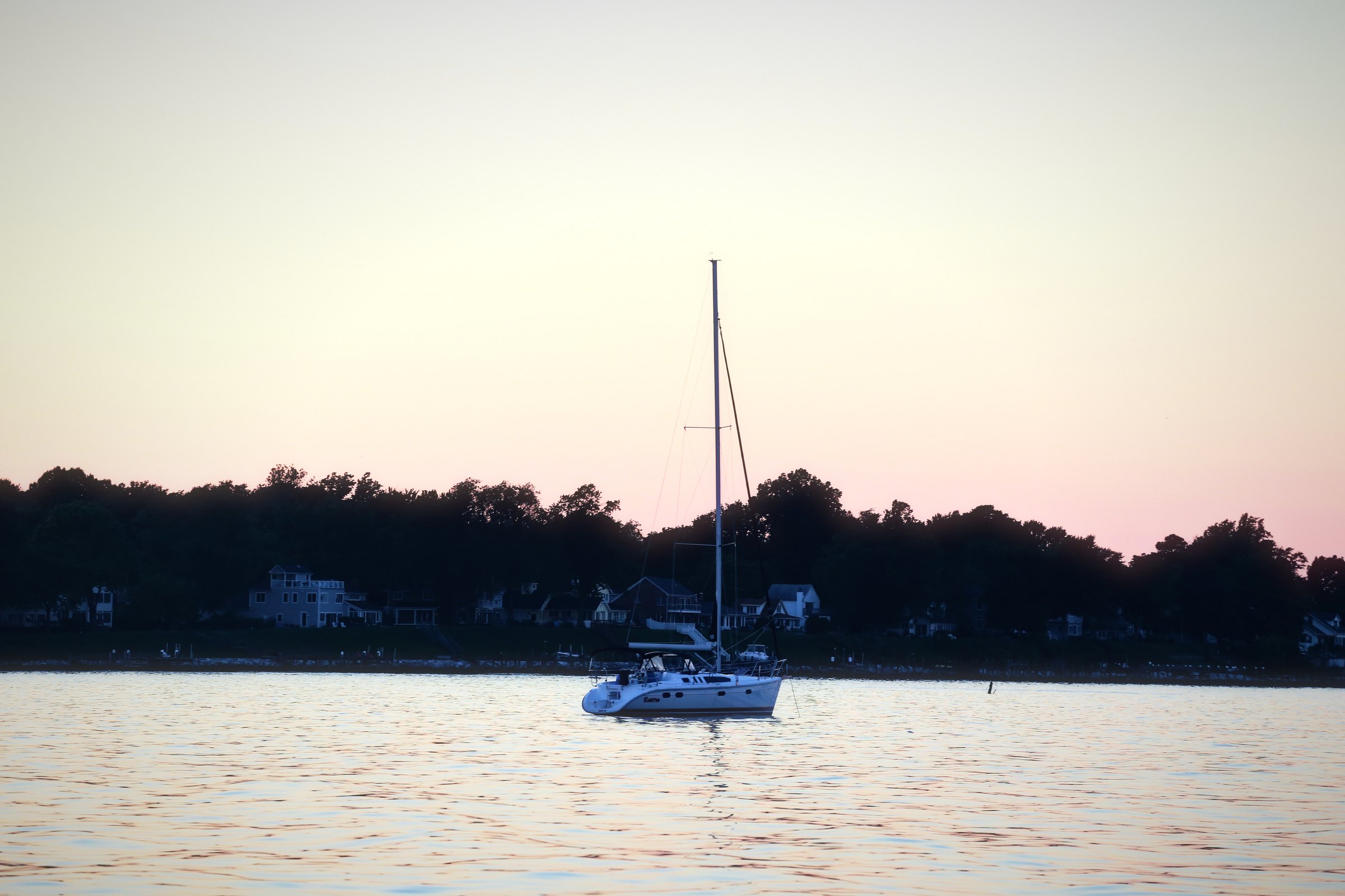 Lone sailboat silhouetted on calm water under a pink and lavender sky.
