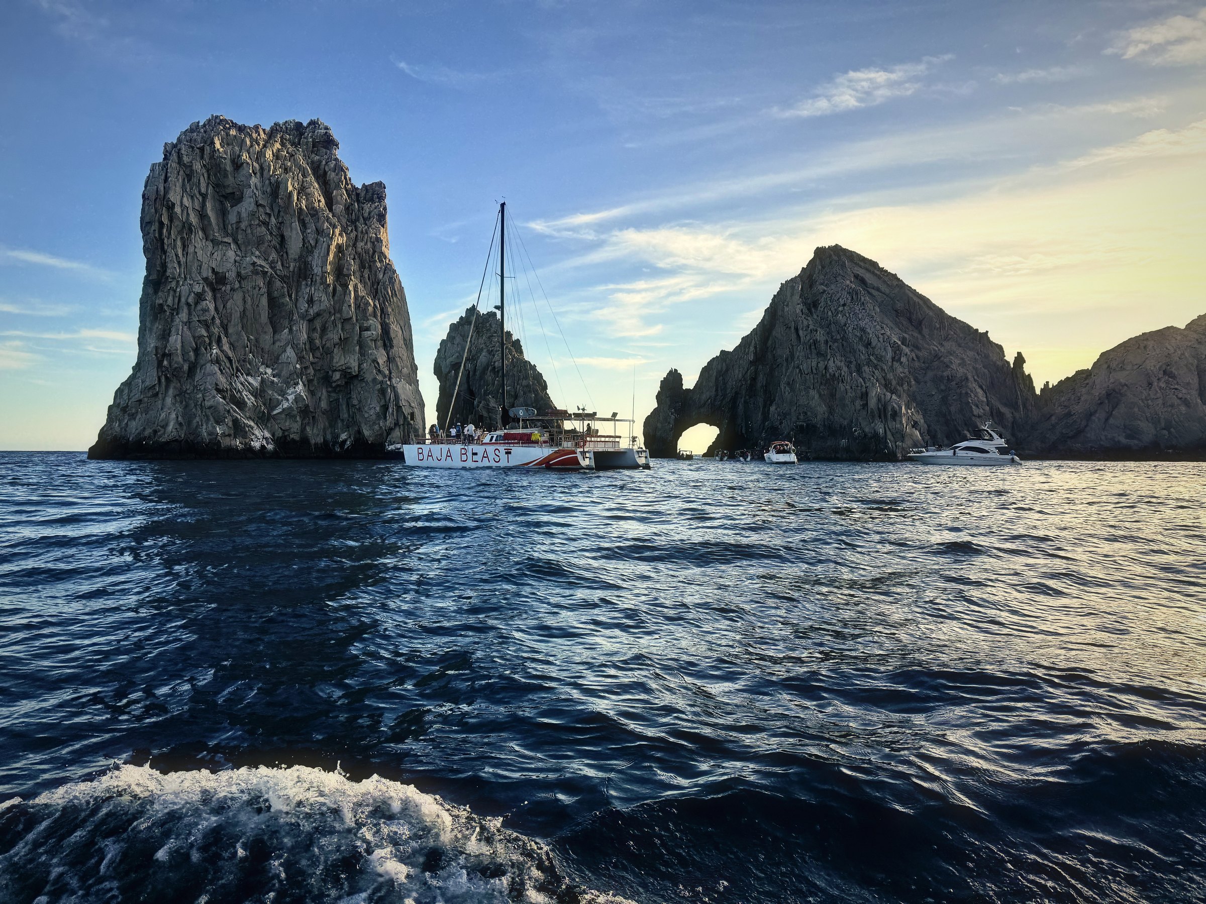 Granite sea stacks rising from the Pacific with a small sailboat among them.