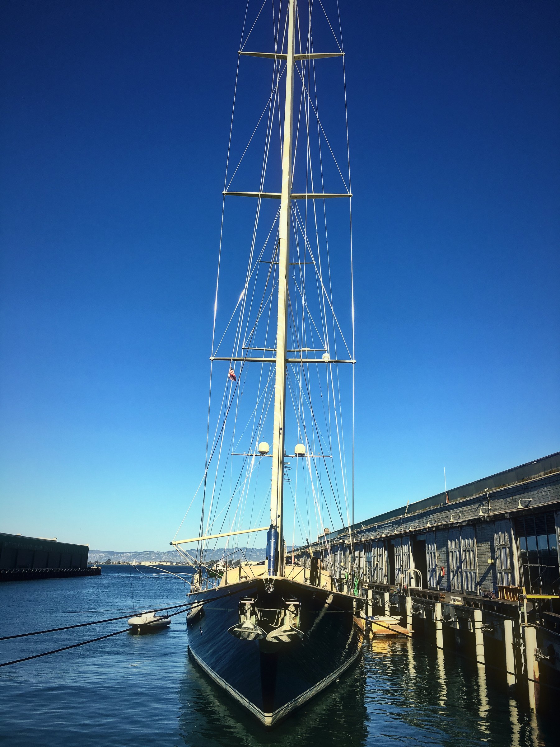 Tall ship masts and rigging towering over a pier against a deep blue sky.