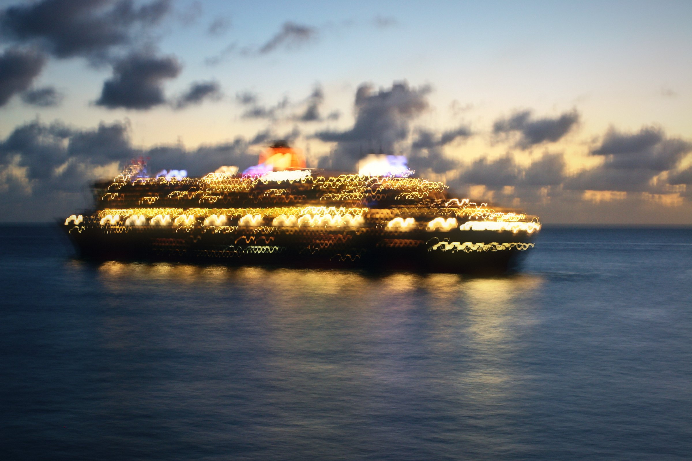 Cruise ship glowing with lights at dusk under dramatic blue clouds.