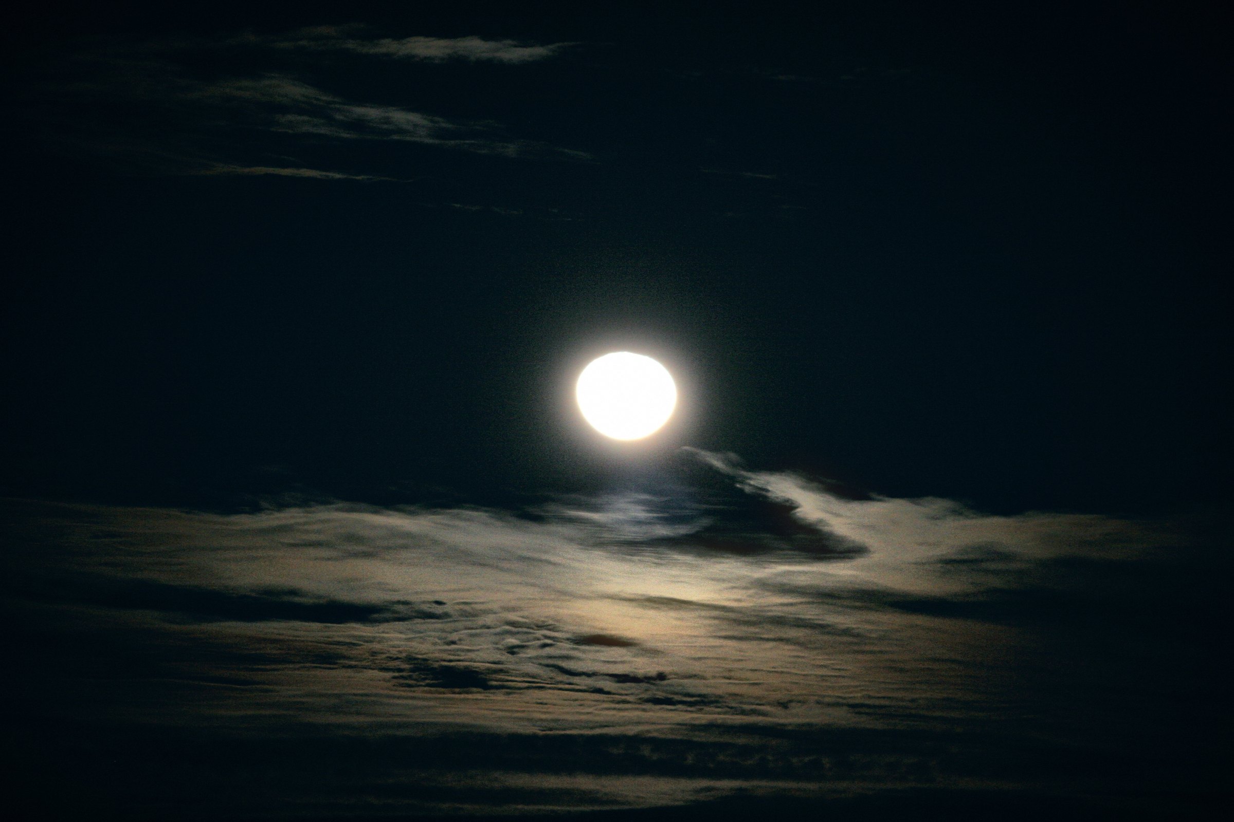 A brilliant moon floating over a dark bank of cloud, the cloud tops edged in silver.