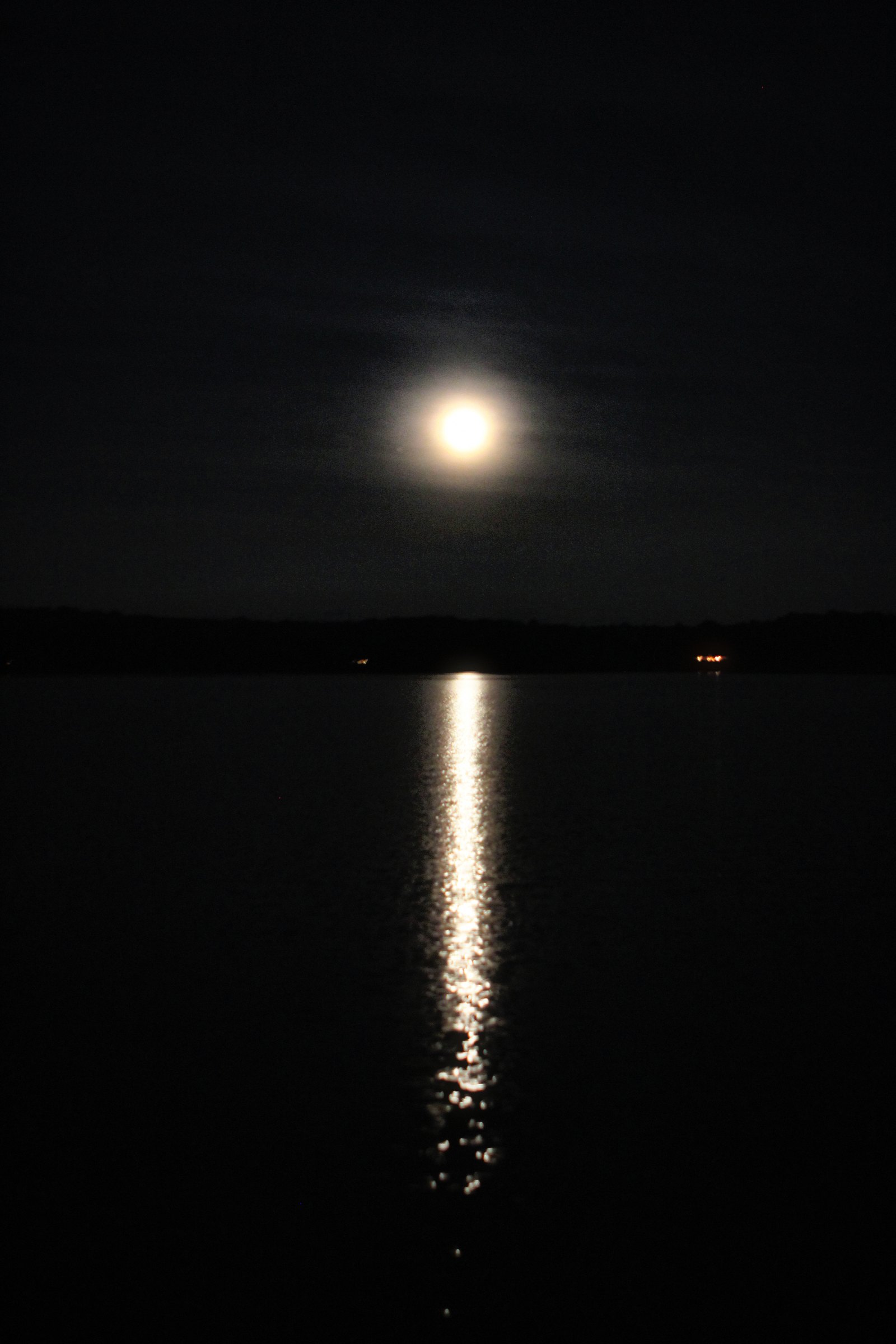 A full moon low over dark water, its reflection running in a long bright path toward the camera.