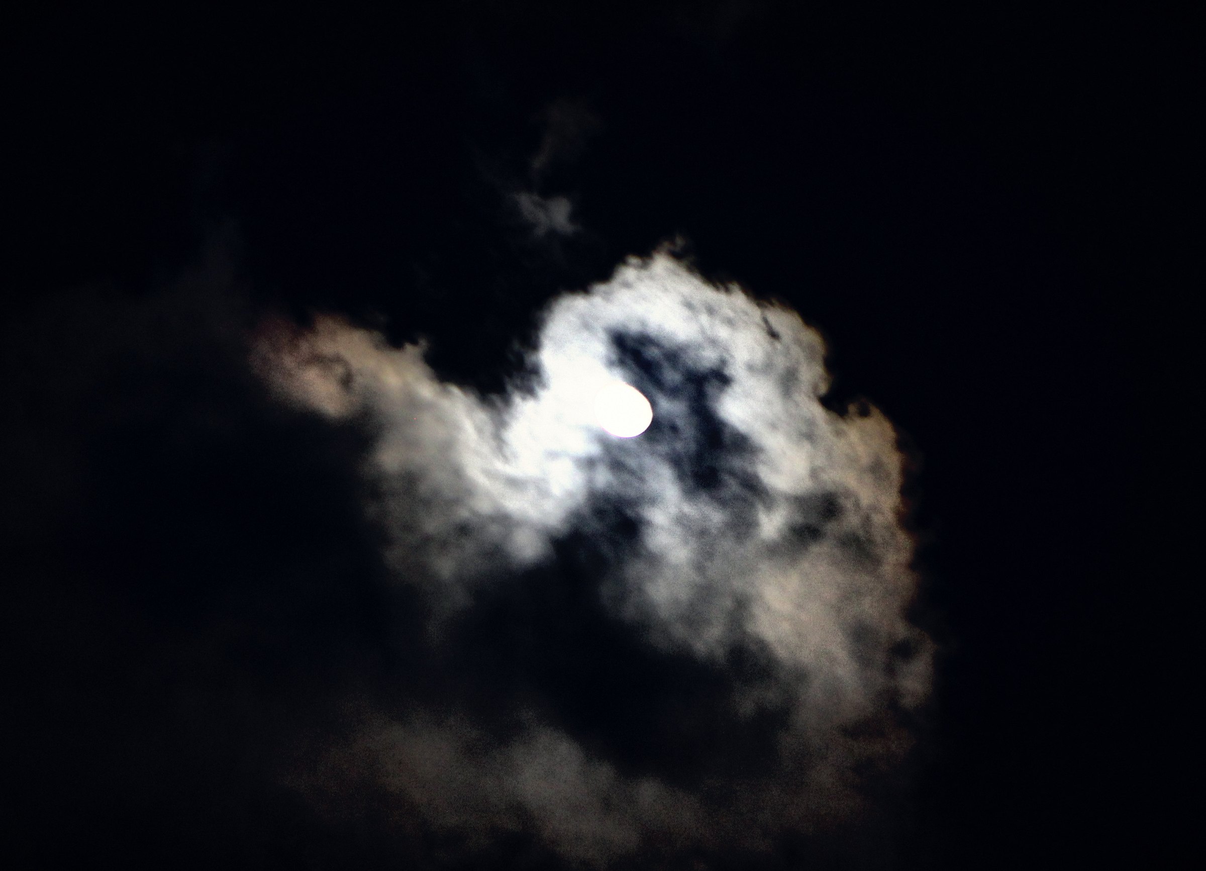 A moon glowing behind a bright, billowing cloud in a black sky, the cloud edges lit white and blue.