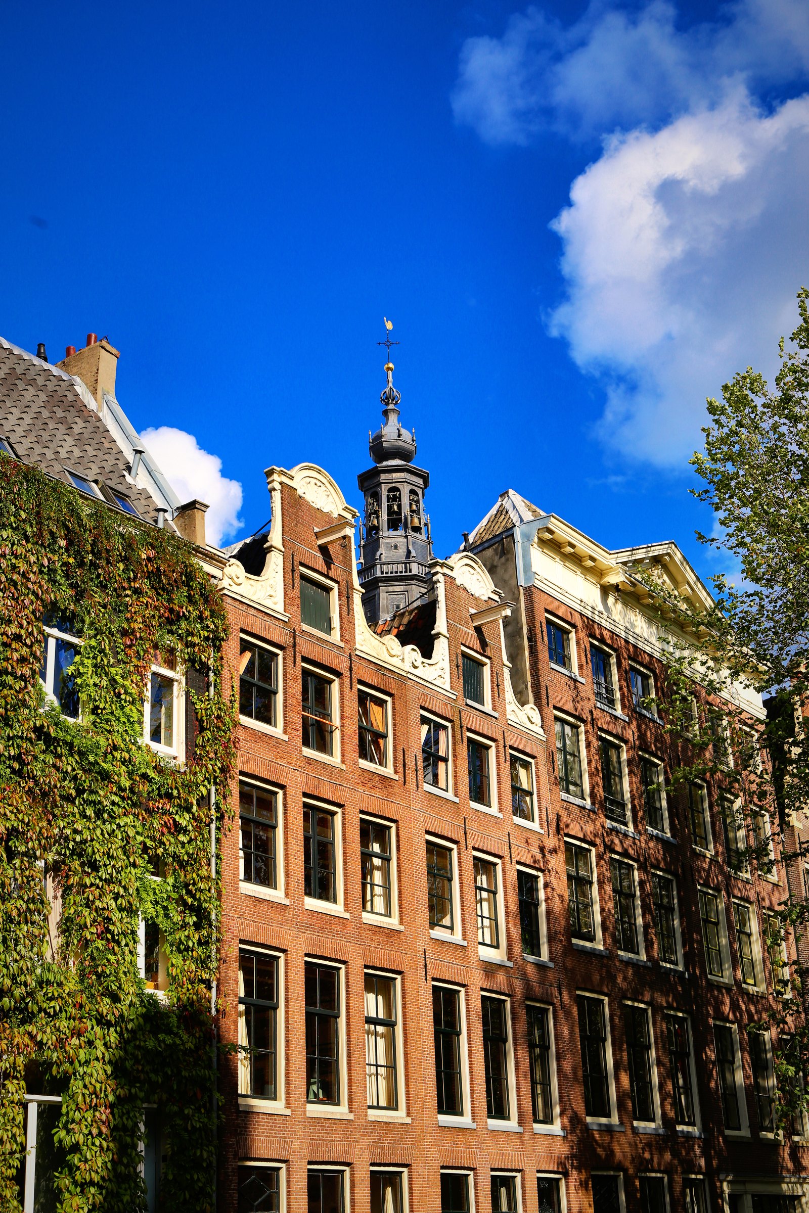 Brick canal houses with stepped and bell gables against a deep blue sky with white cloud.