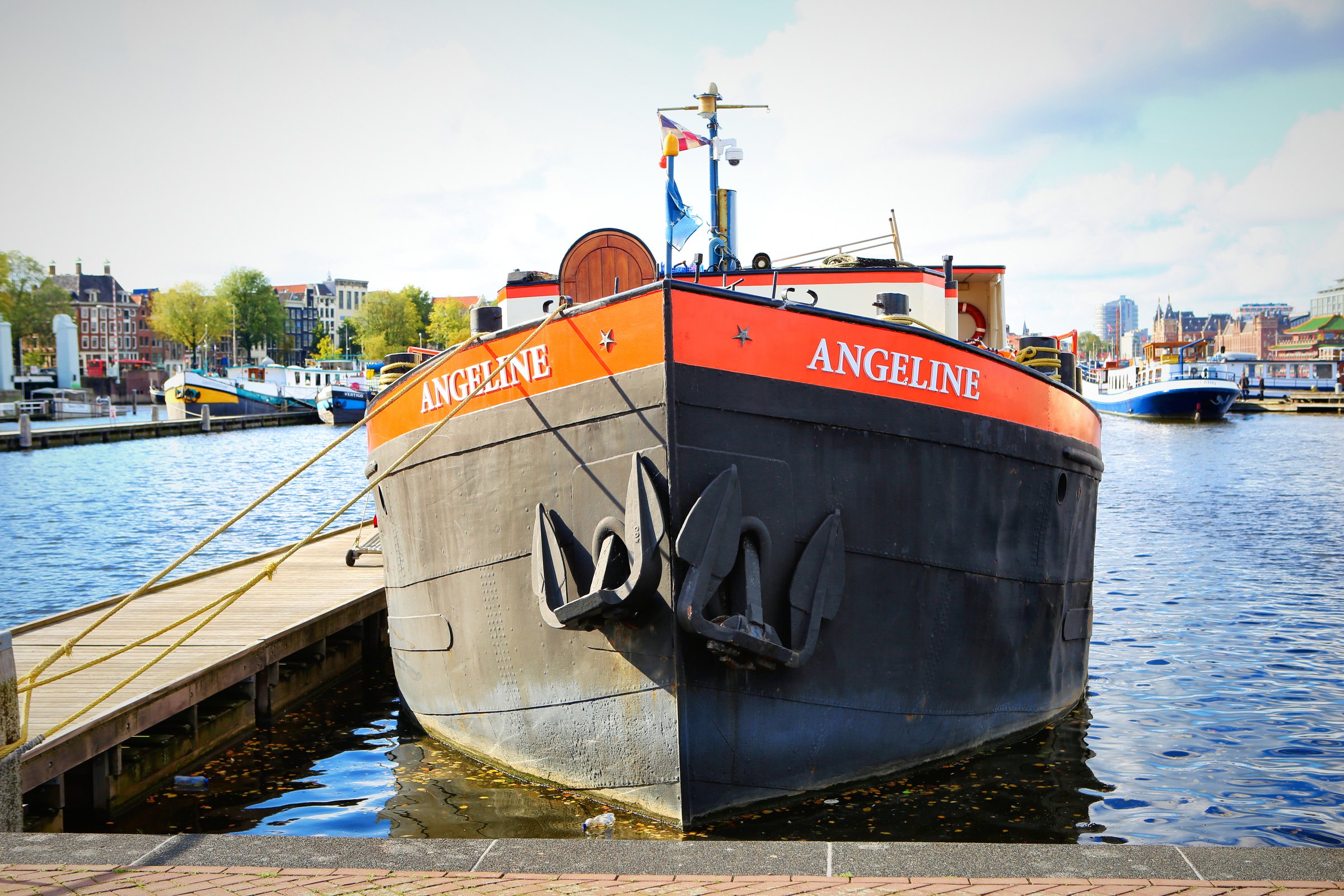 A black barge with an orange stripe moored on the waterfront.