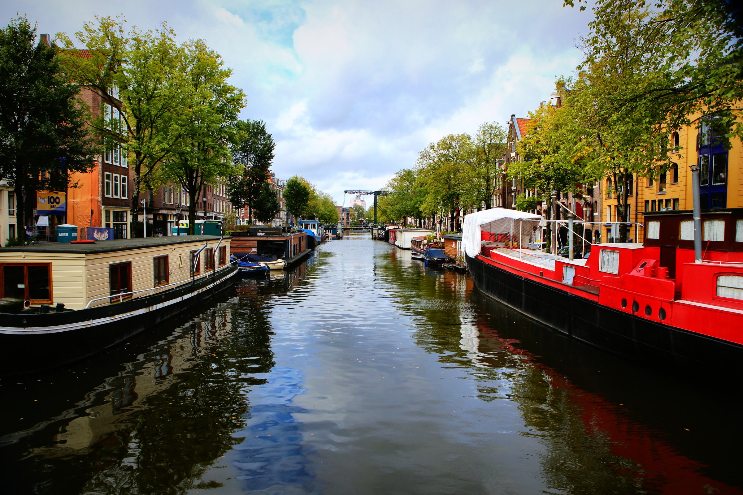 Houseboats moored along a tree-lined canal with a red boat on the right.