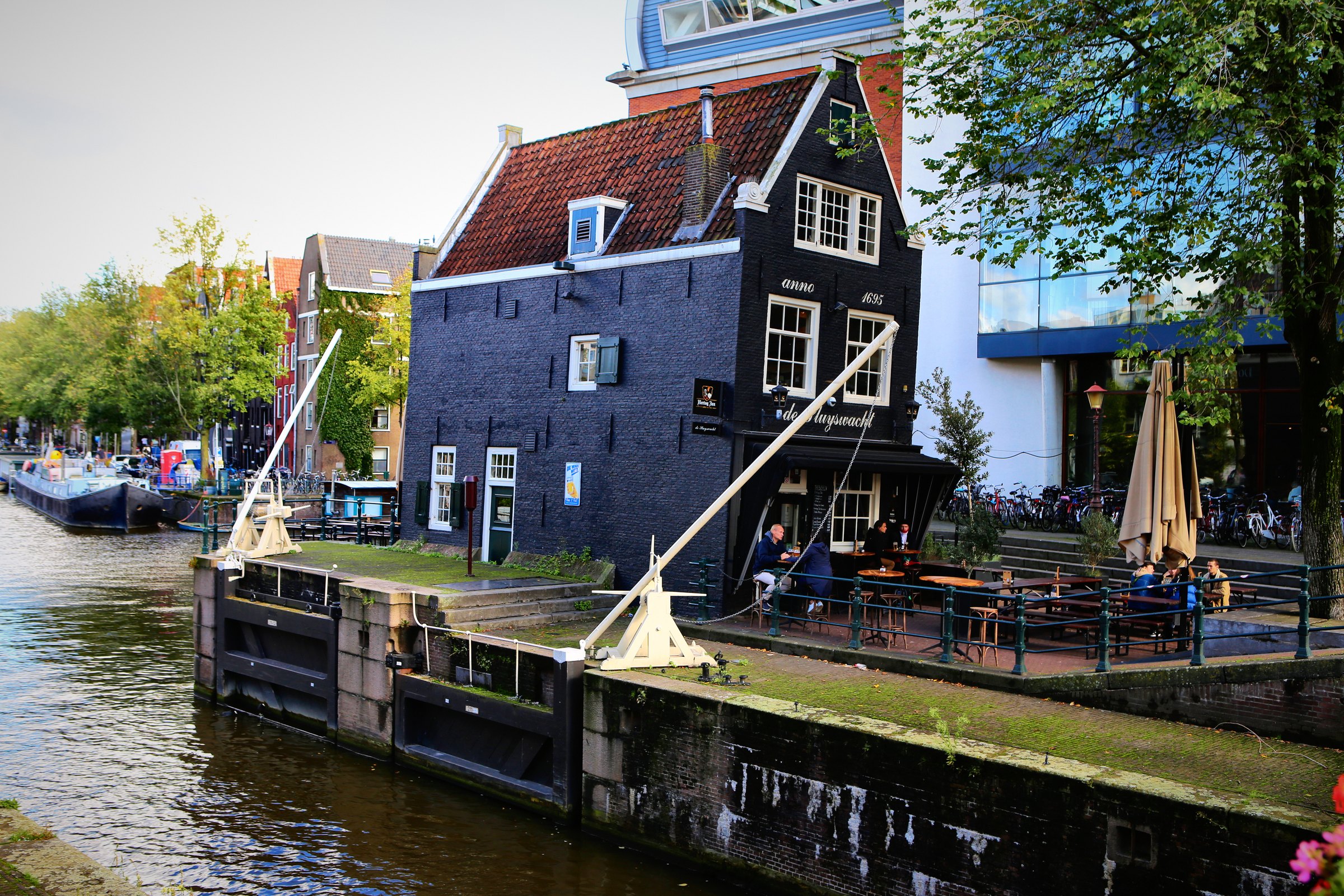 A dark wooden house beside the water with a terrace and boats below.