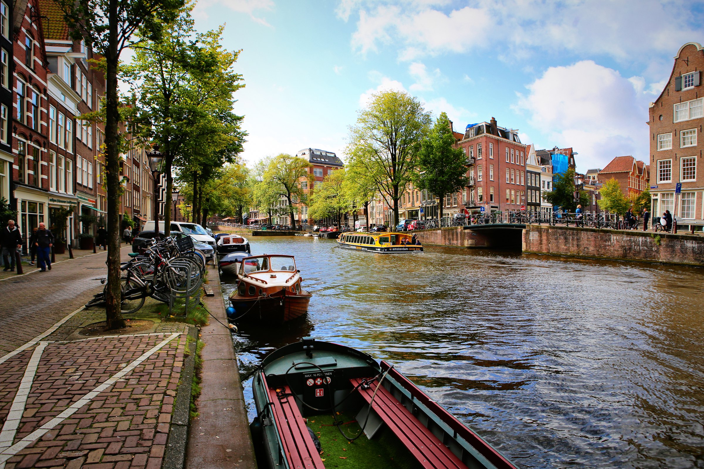 A brick quayside running beside a canal of moored boats under bright clouds.