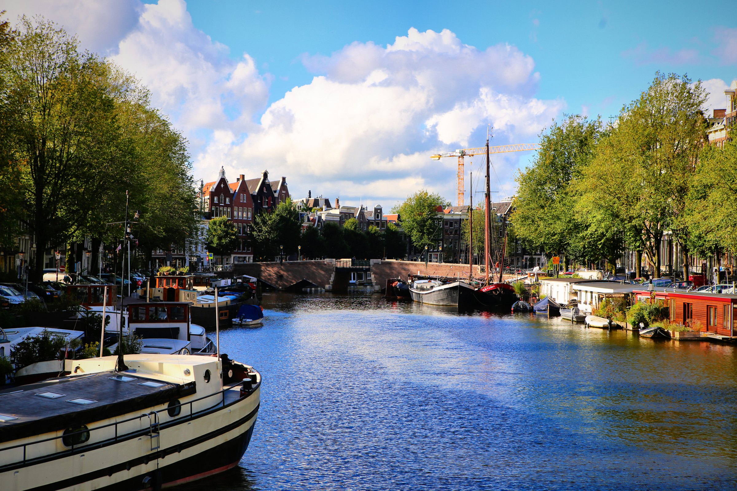 Wide water with houseboats and a lifting bridge under big clouds.