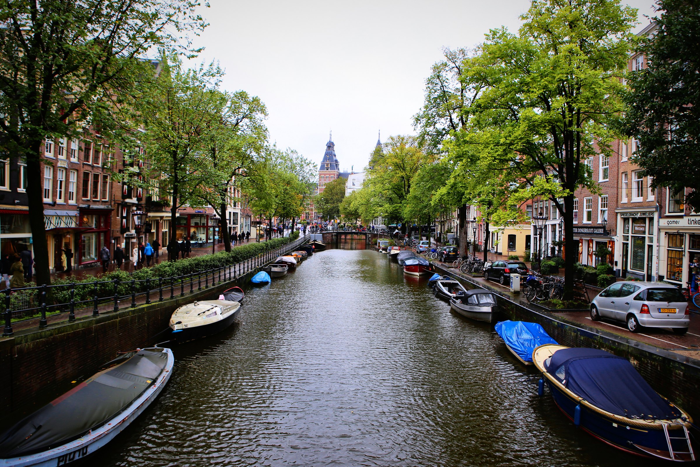 A long straight canal lined with trees and moored boats, a church tower at the far end.