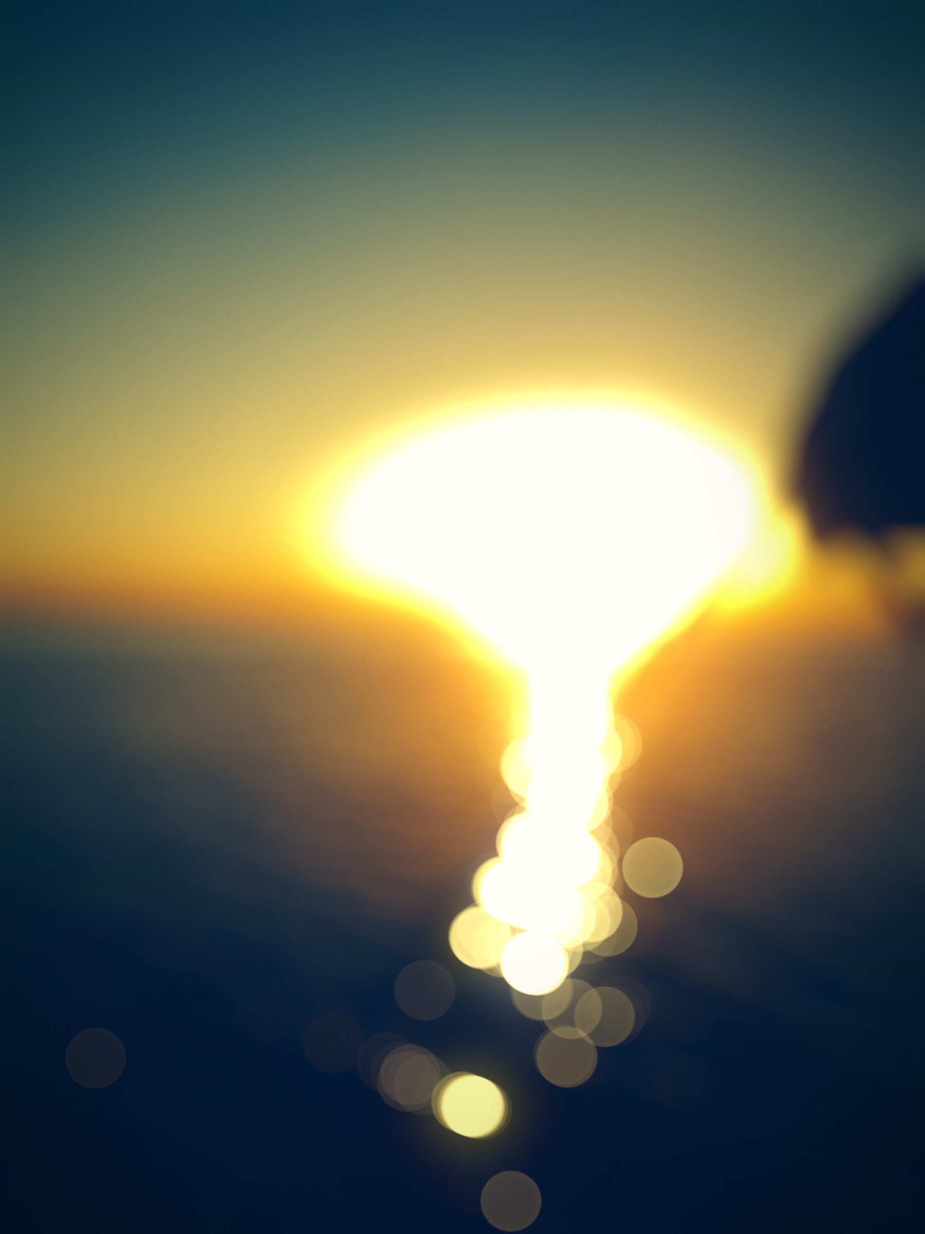 Setting sun and its reflection melting into gold bokeh over blue water.
