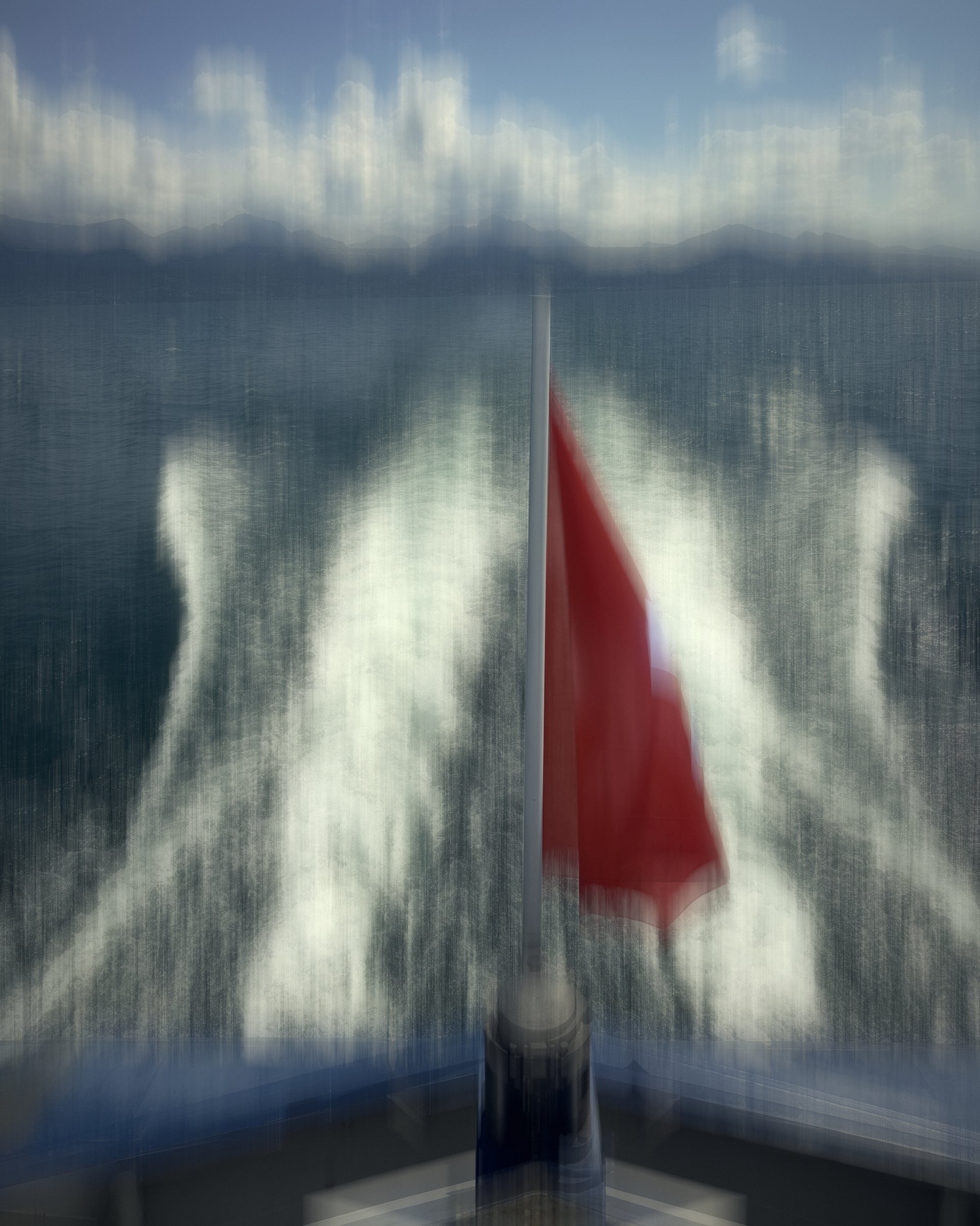 Abstract motion blur of a boat's white wake and red flag on blue water.