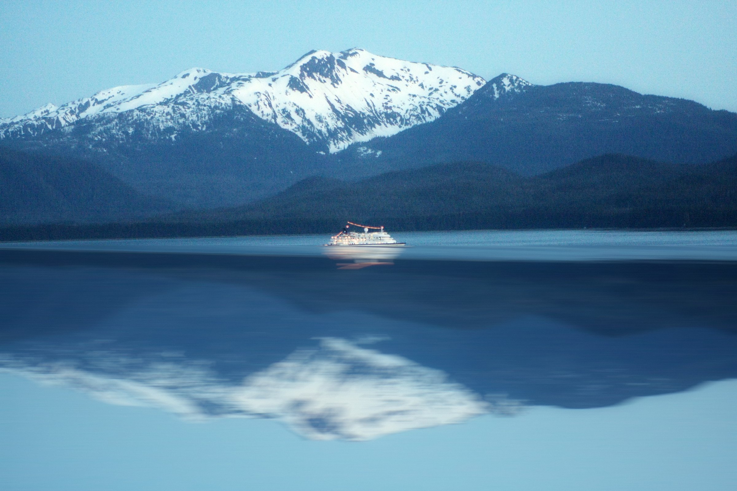 Mirrored image of a white ferry and snowy peaks reflected in a deep blue lake.
