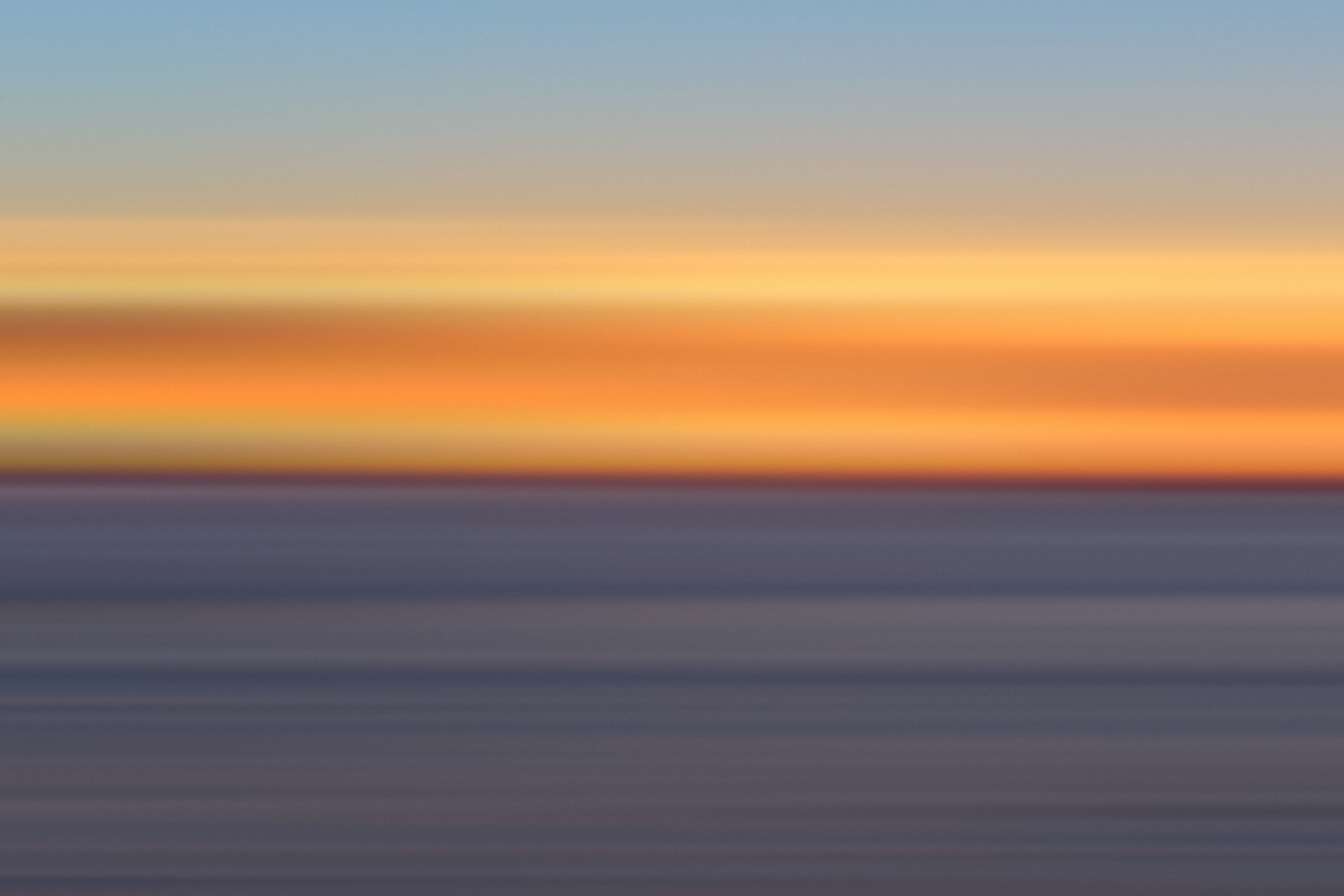 Horizontal color bands of tangerine, blue and slate from a sunset over the sea.