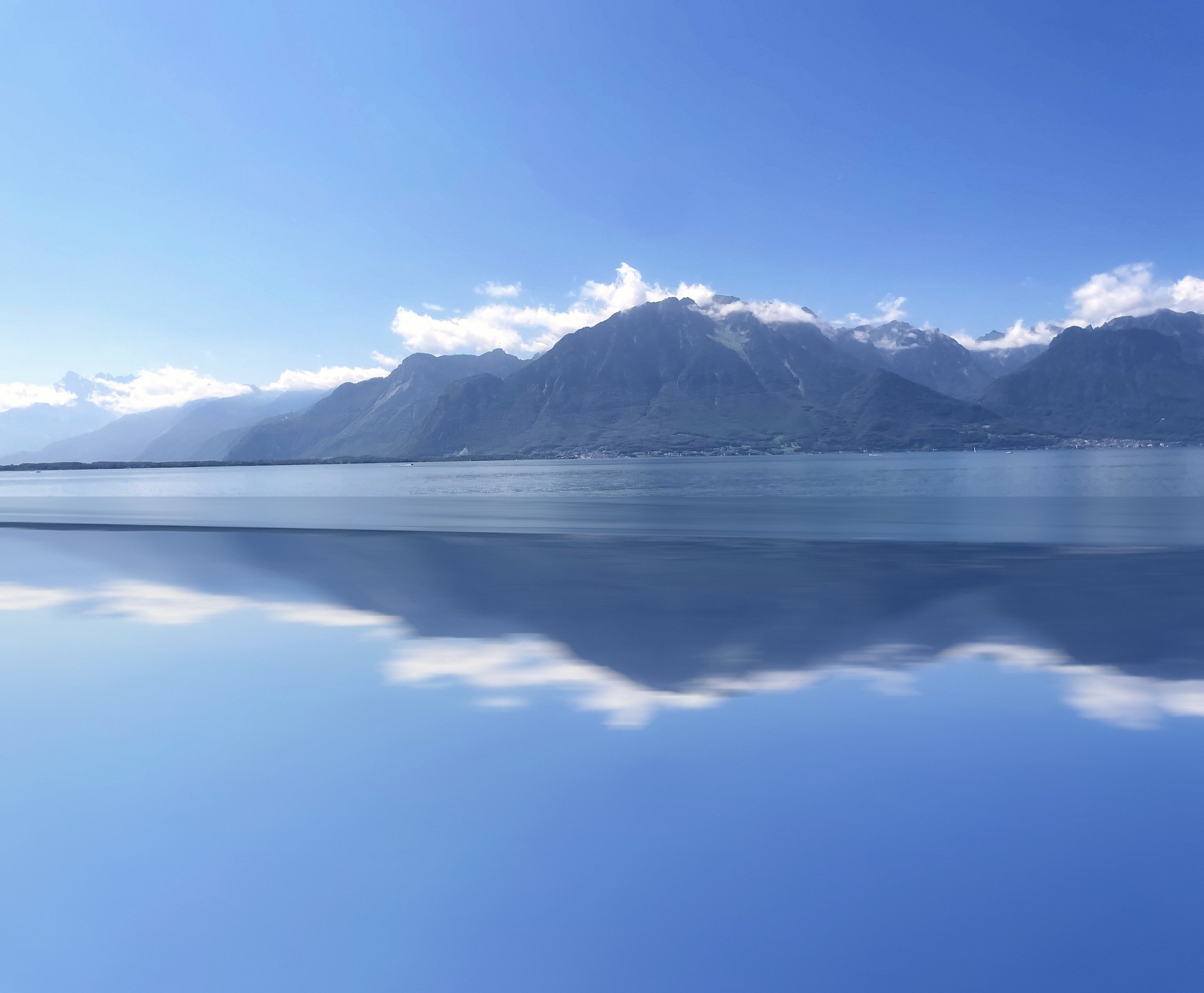 Mirrored lake and clouded mountain peaks in layers of blue.
