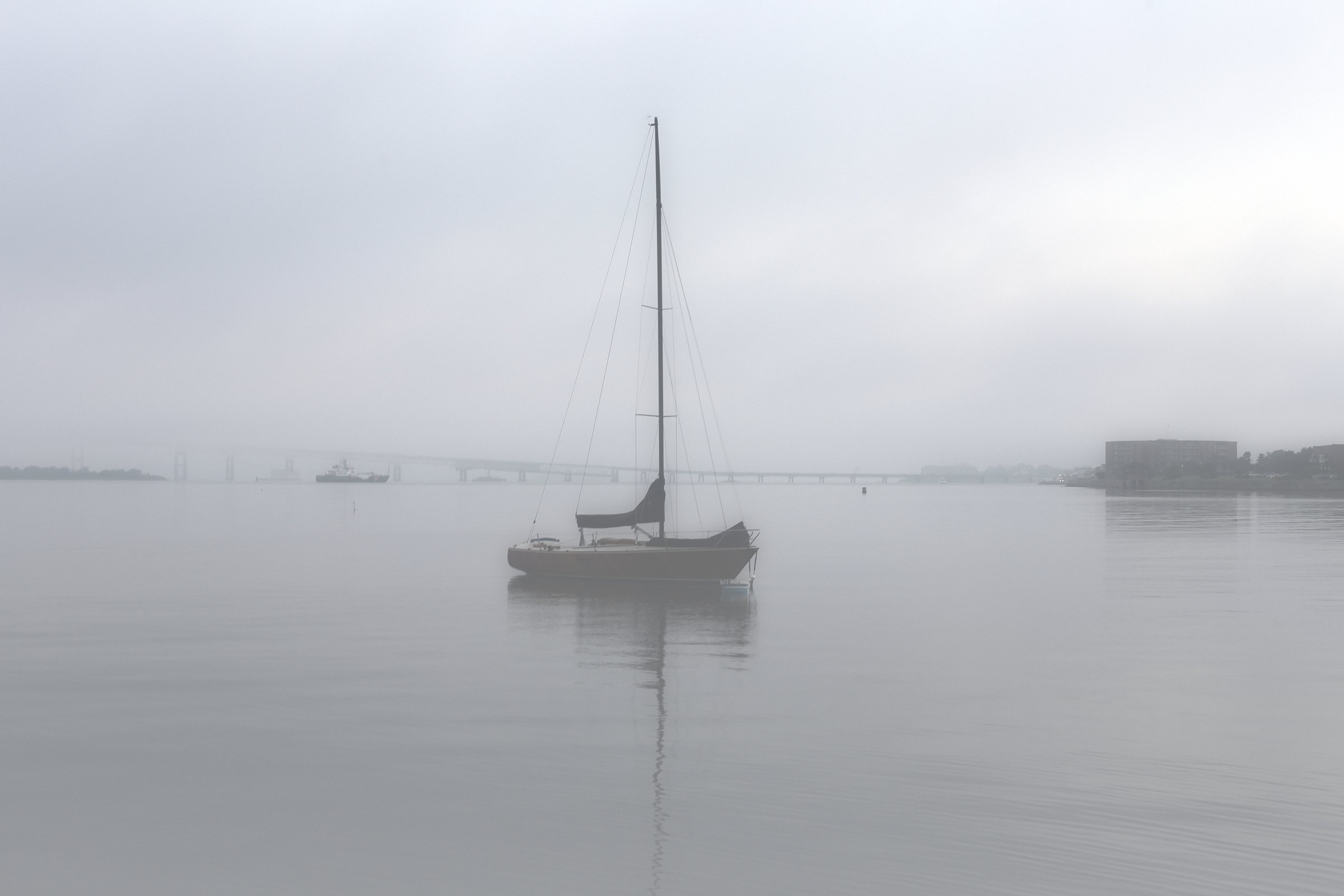 High-key misty image of a lone sailboat on pale water.