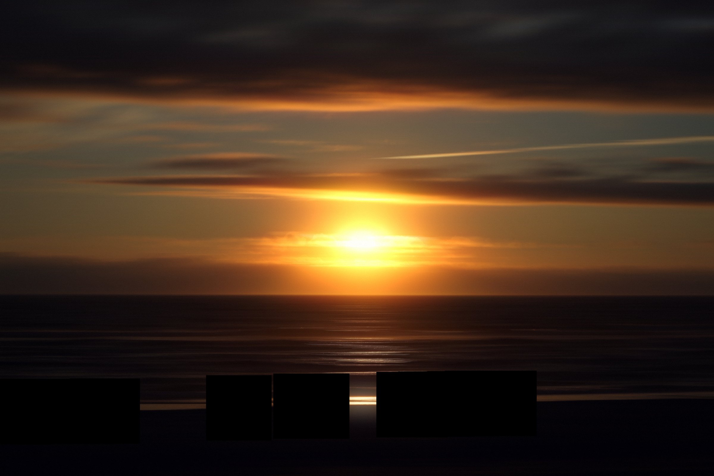 Ocean sunset streaked sideways into ribbons of gold and dark blue.